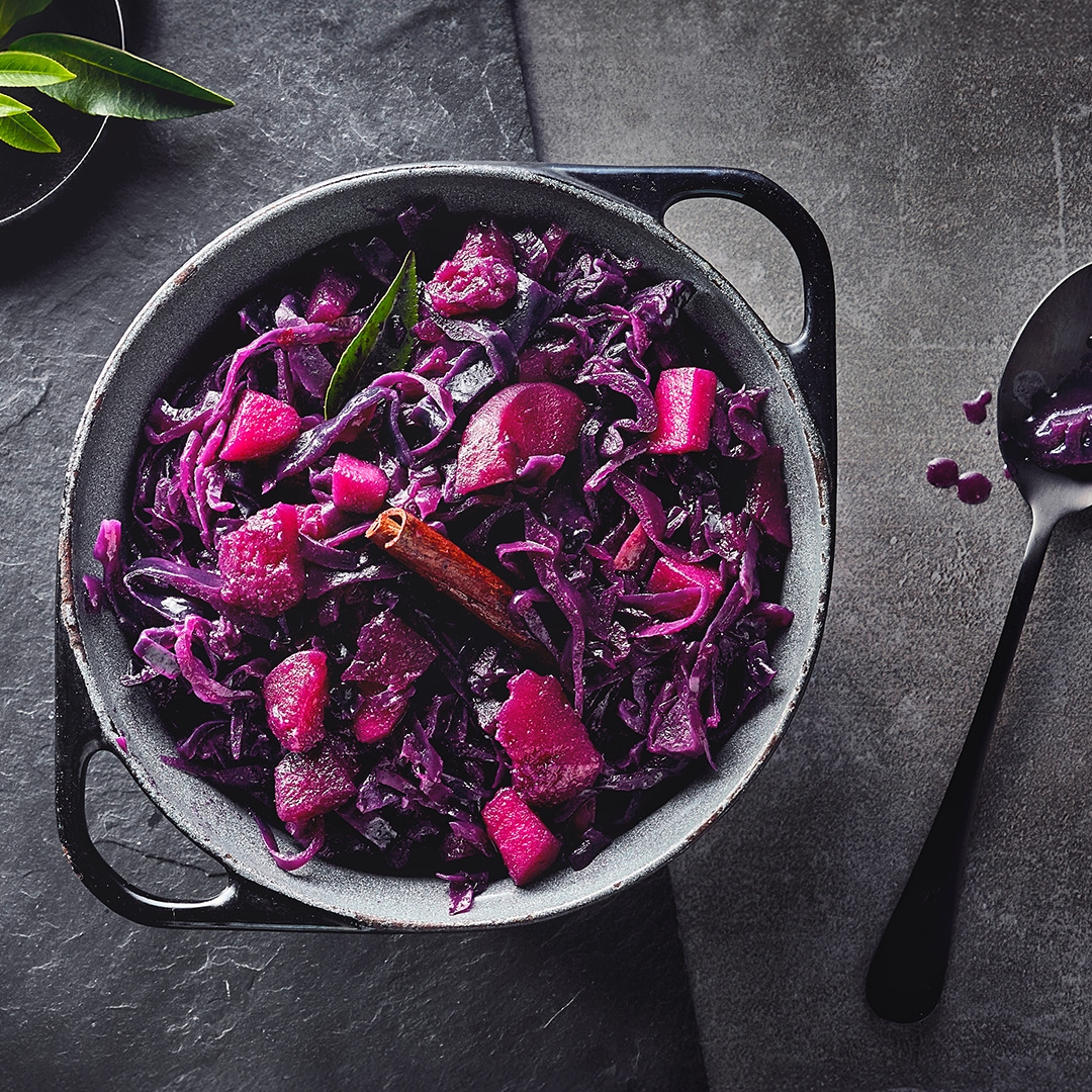 Ein gusseiserner Topf mit saftigem Rotkohl, verfeinert mit einer Stange Zimt und einem Lorbeerblatt