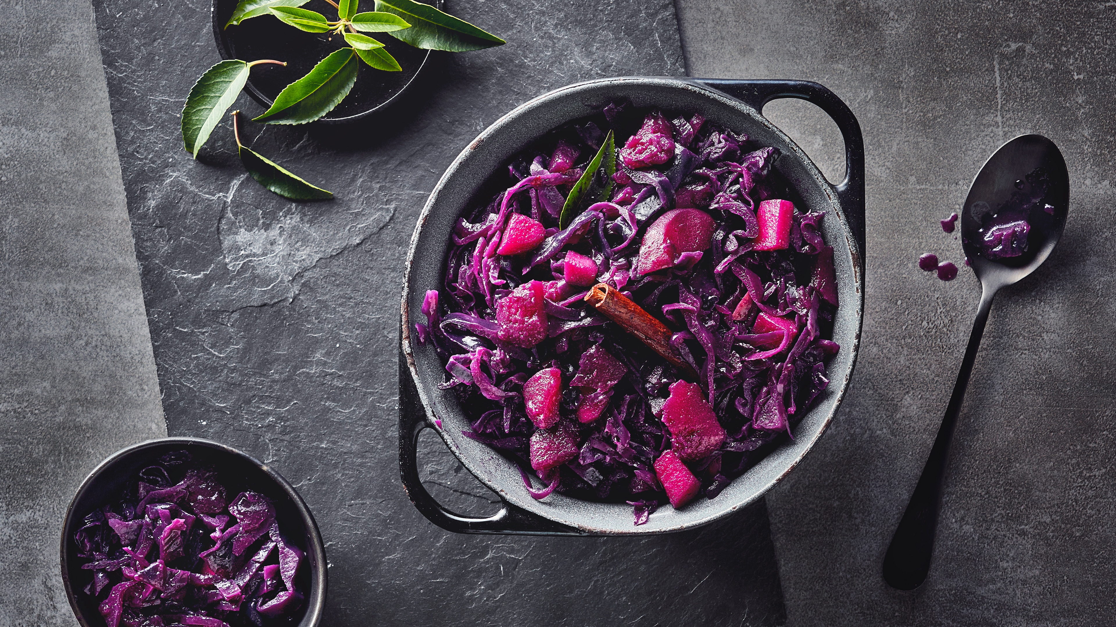 Rezept für Apfelrotkohl Ein gusseiserner Topf mit saftigem Rotkohl, verfeinert mit einer Stange Zimt und einem Lorbeerblatt