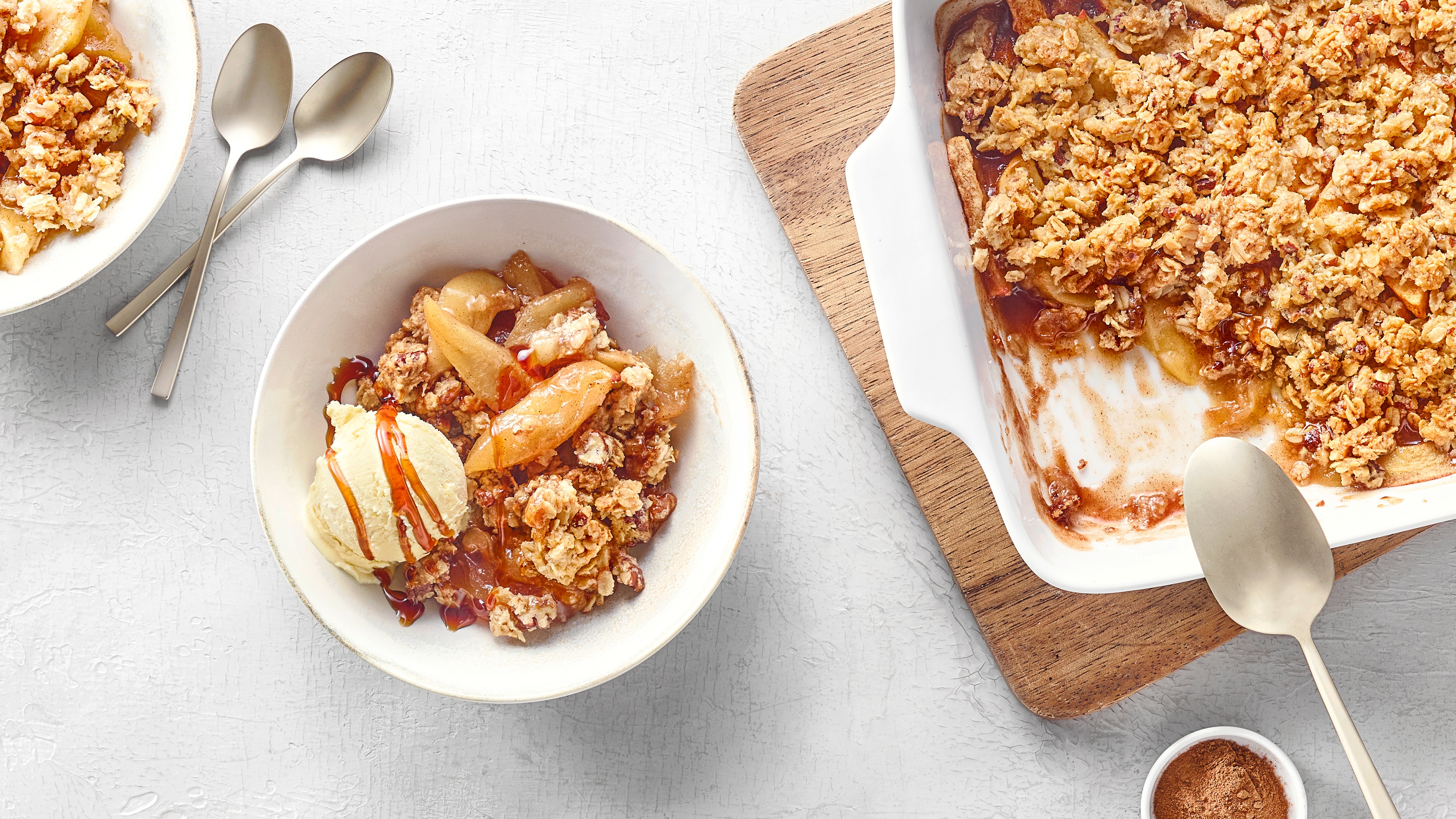 Auflaufform mit gebackenem Apfel und krümeligem Topping. Daneben dies im Schälchen mit einer Kugel hellem Eis und Soße.