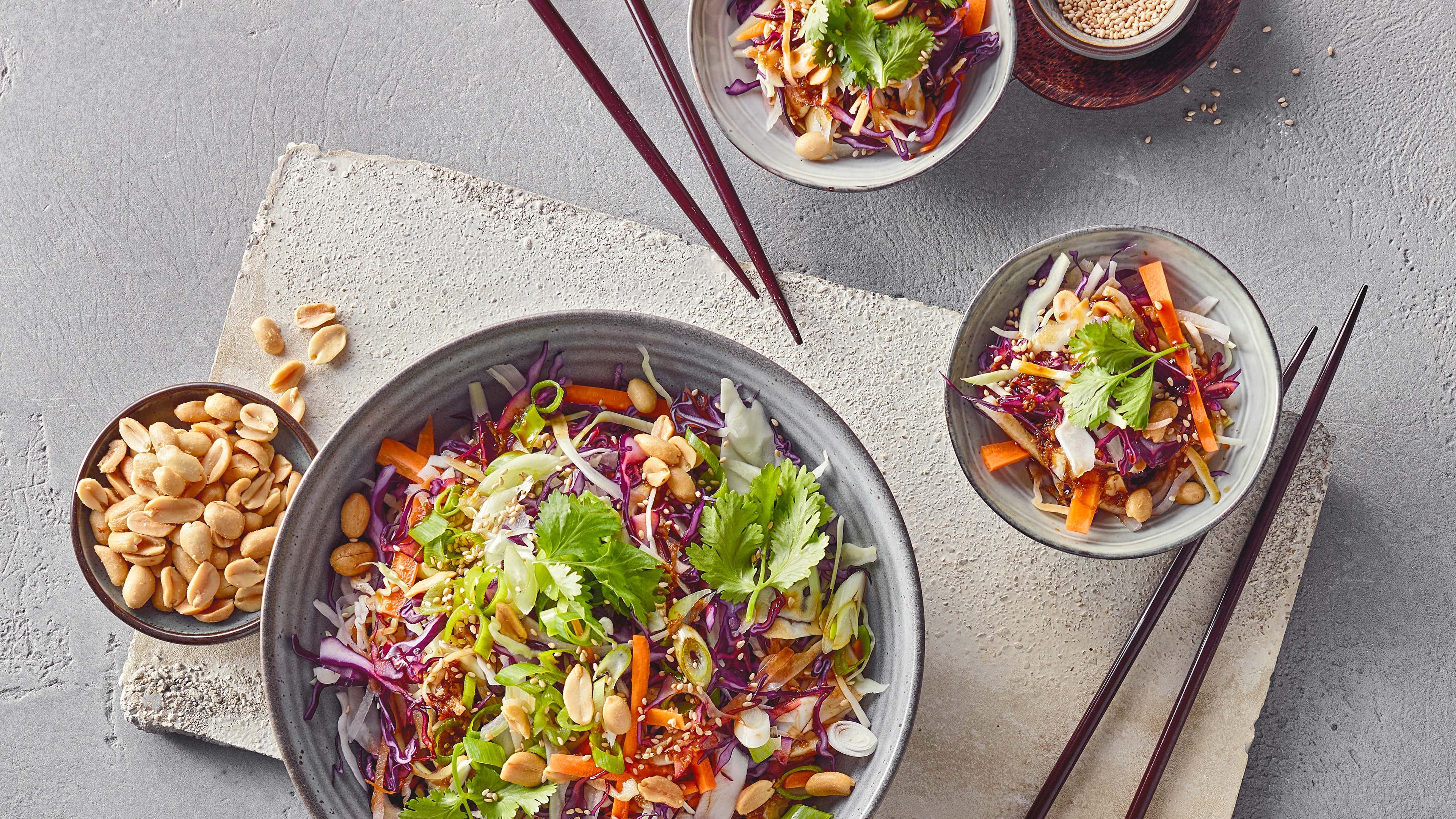 Rezept für Asiatischen Krautsalat Eine Schale mit Karottenstreifen, Rotkohl, Weißkohl, Frühlingszwiebeln und Erdnüssen, garniert mit Korianderblättern