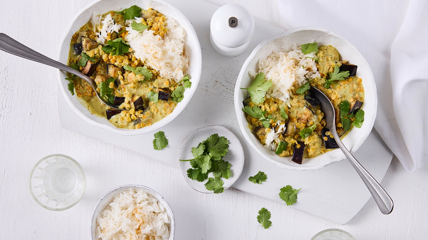 Stückiges Linsen-Auberginen-Gericht mit Reis in weißer Schale, daneben Schälchen mit Koriander und Reis