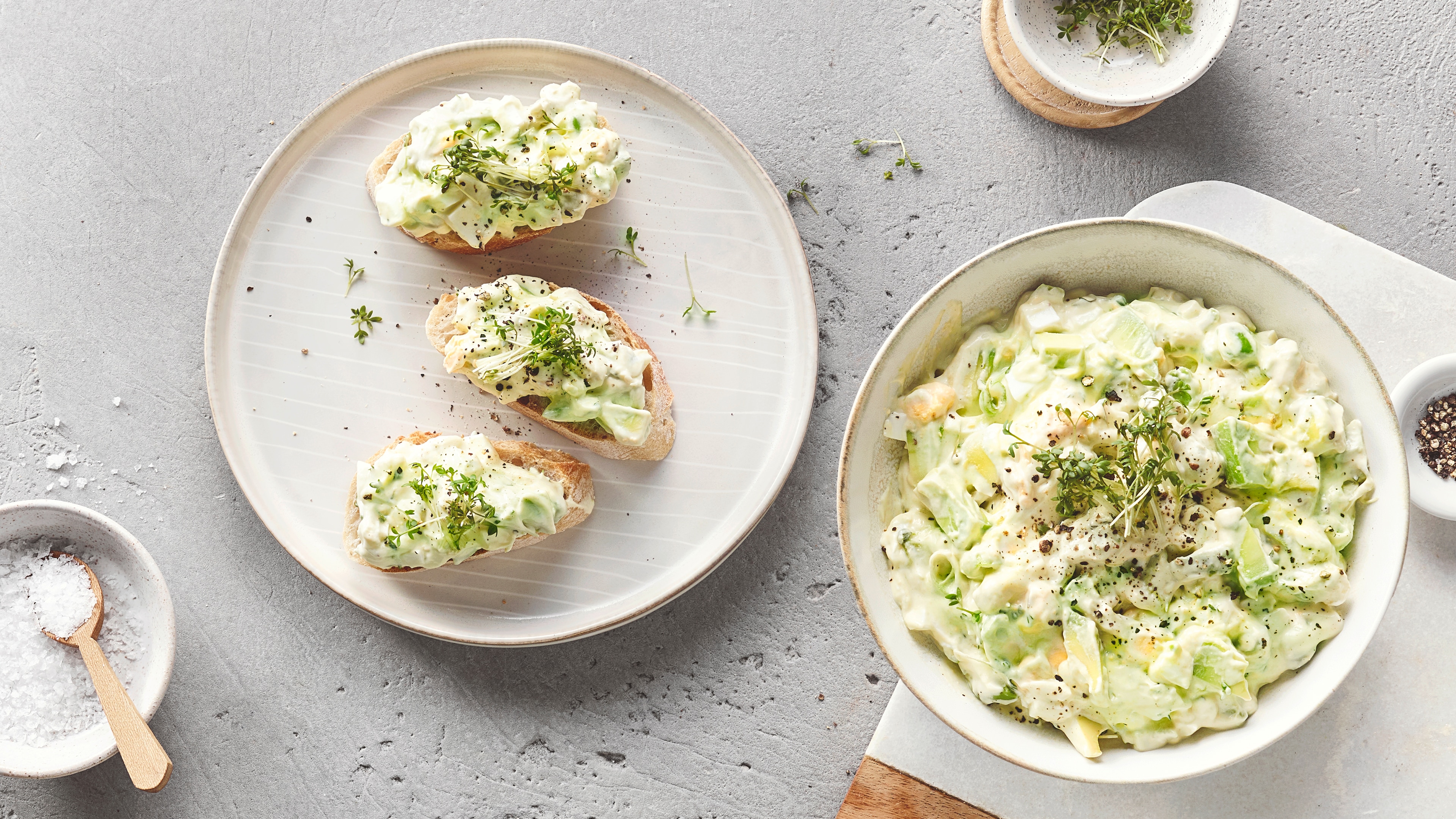 Ein Teller mit drei Brotscheiben, belegt mit weißer Creme, grünen Avocadostücken, schwarzem Pfeffer und frischer Kresse.