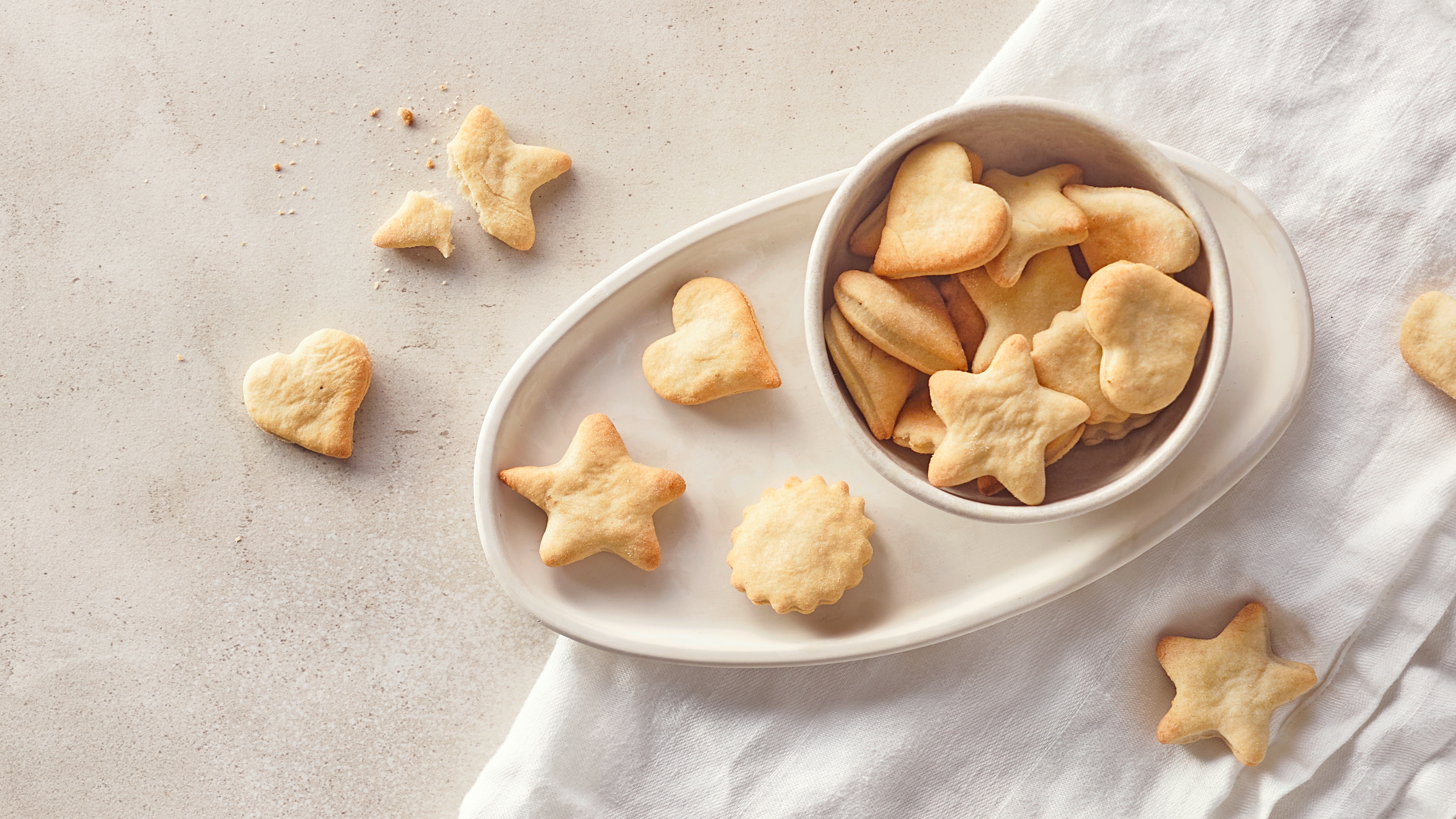 Rezept für selber gebackene Babykekse Ein Schälchen und eine Tablett, befüllt mit kleinen Butterkeksen in Form von Sternen, Herzen und Vielecken