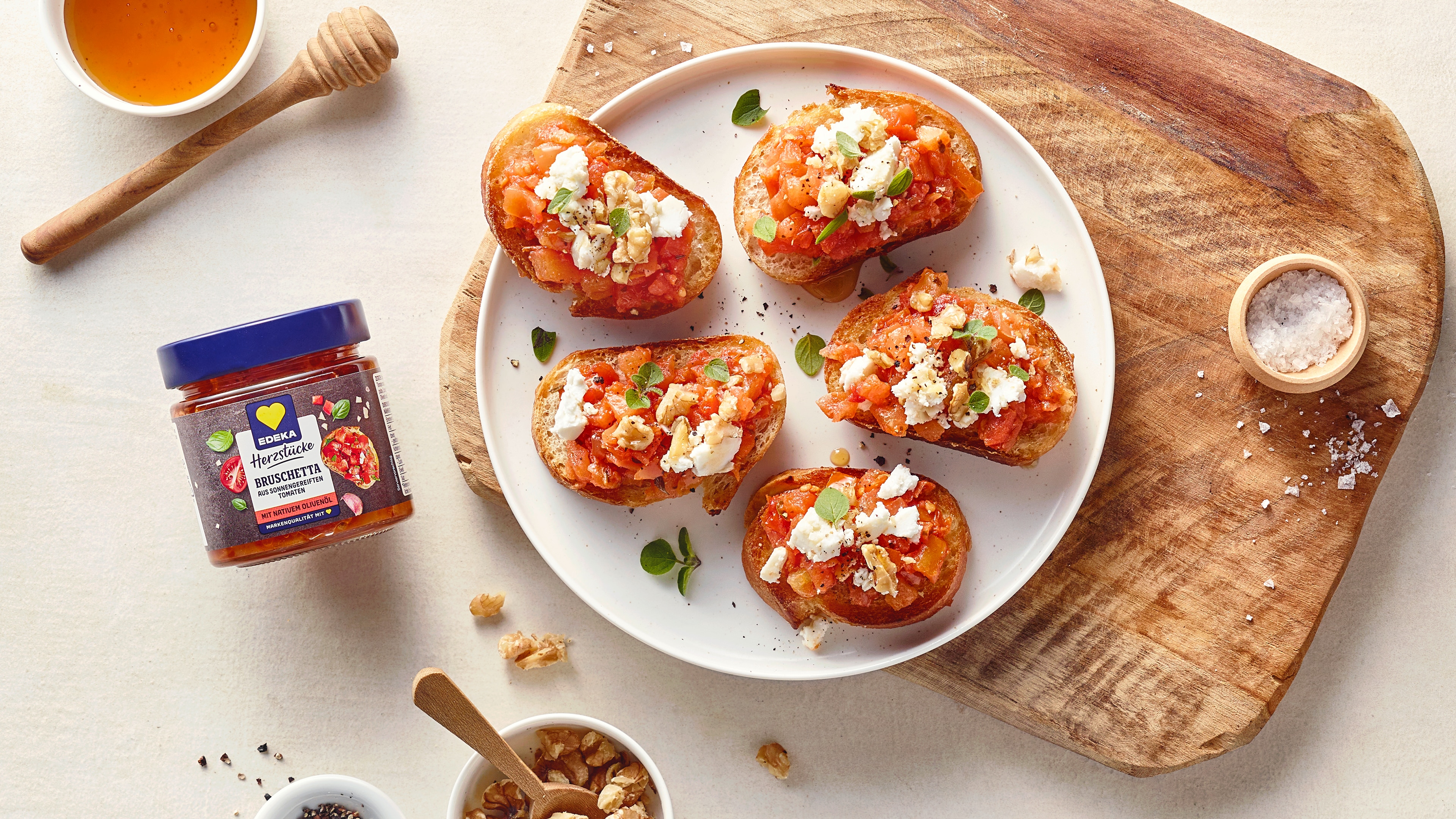 Ein Teller mit fünf gerösteten Brotscheiben, belegt mit Tomatenwürfeln, zerbröckeltem Käse, Nüssen und grünen Blättern