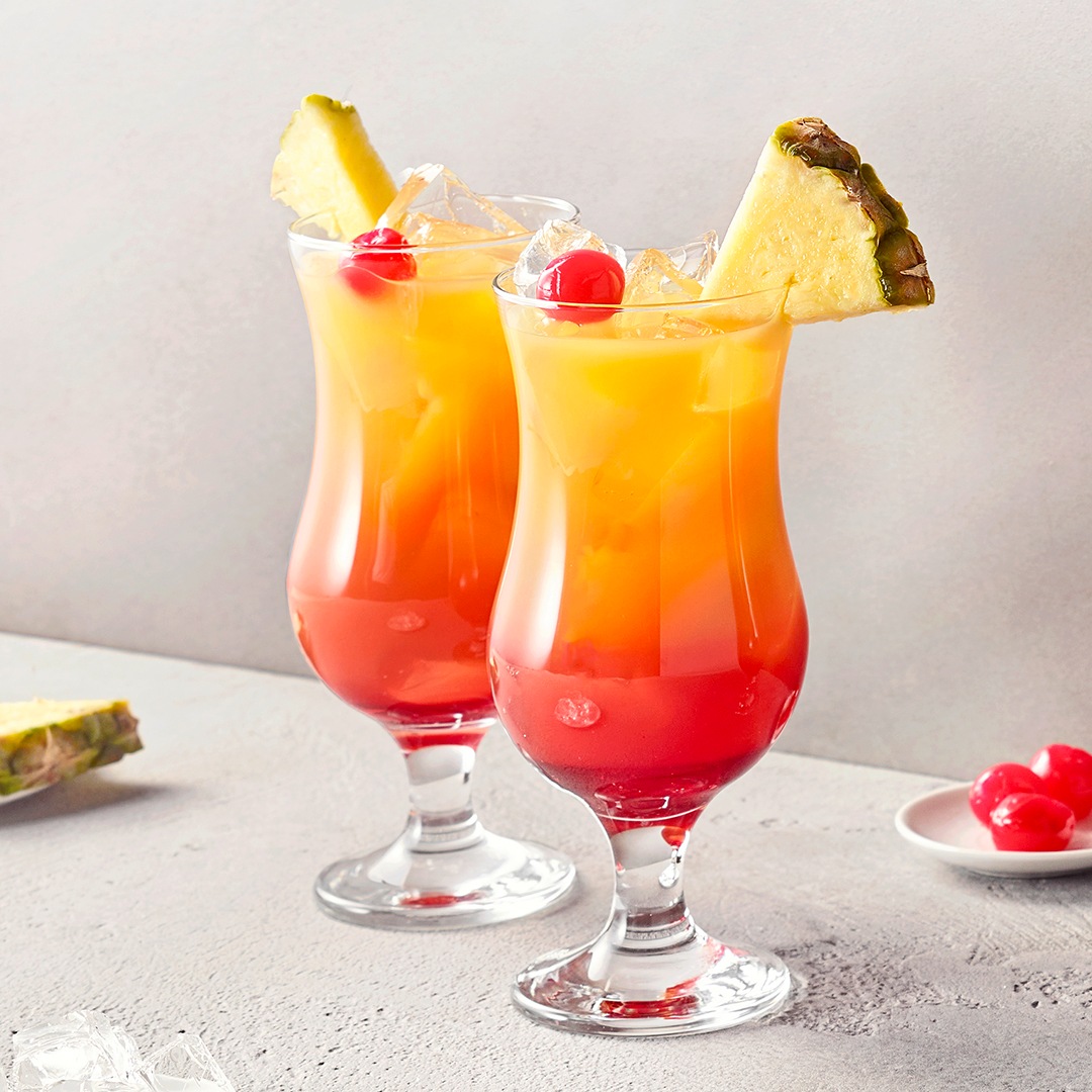 Zwei Gläser mit rot-gelber Flüssigkeit, Eiswürfeln, Kirsche und jeweils einem Ananasstück
