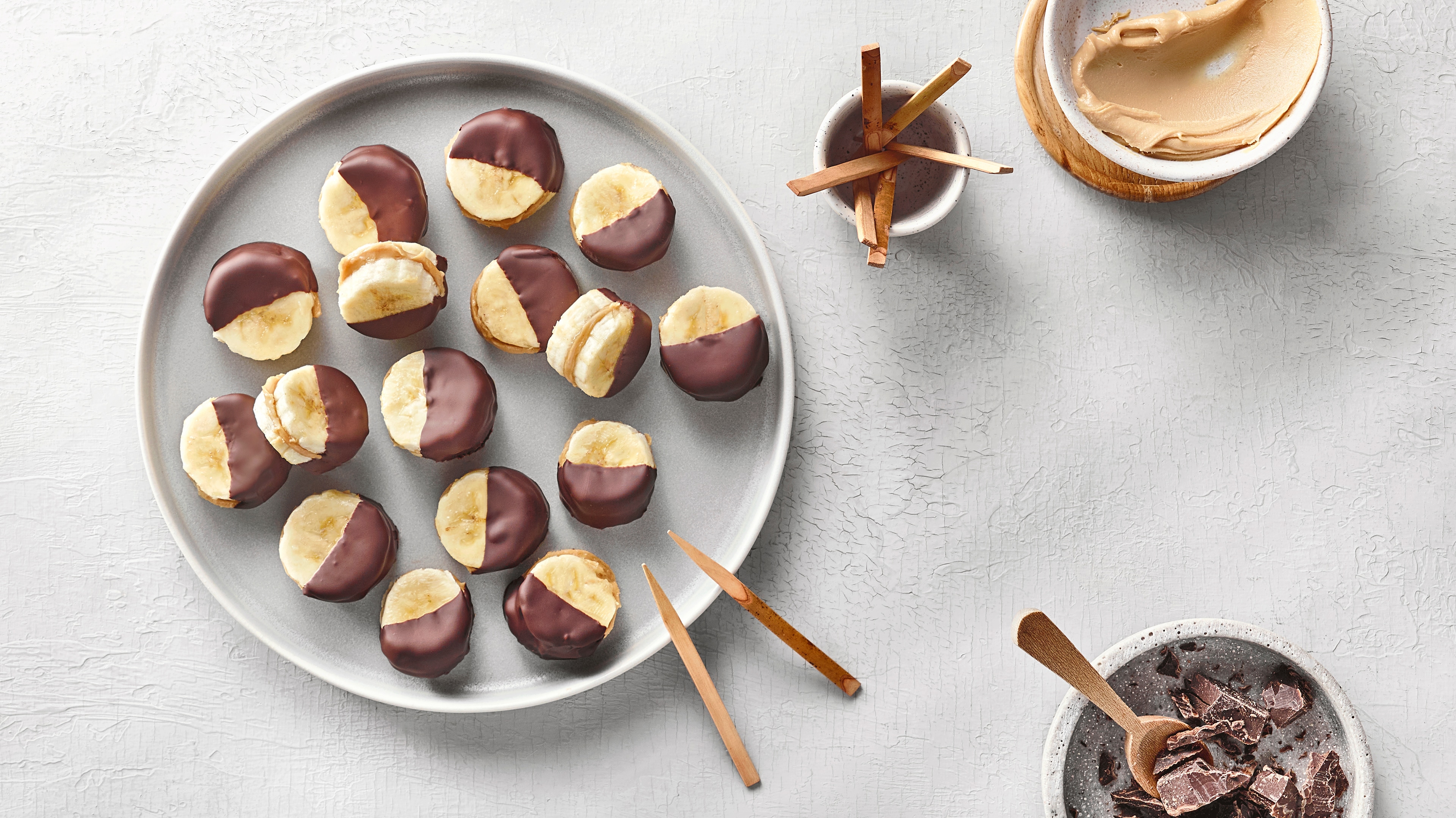 Kleine Banana Bites aus zwei Bananenscheiben, gefüllt mit Erdnussbutter und zur Hälfte in Schokolade getaucht.