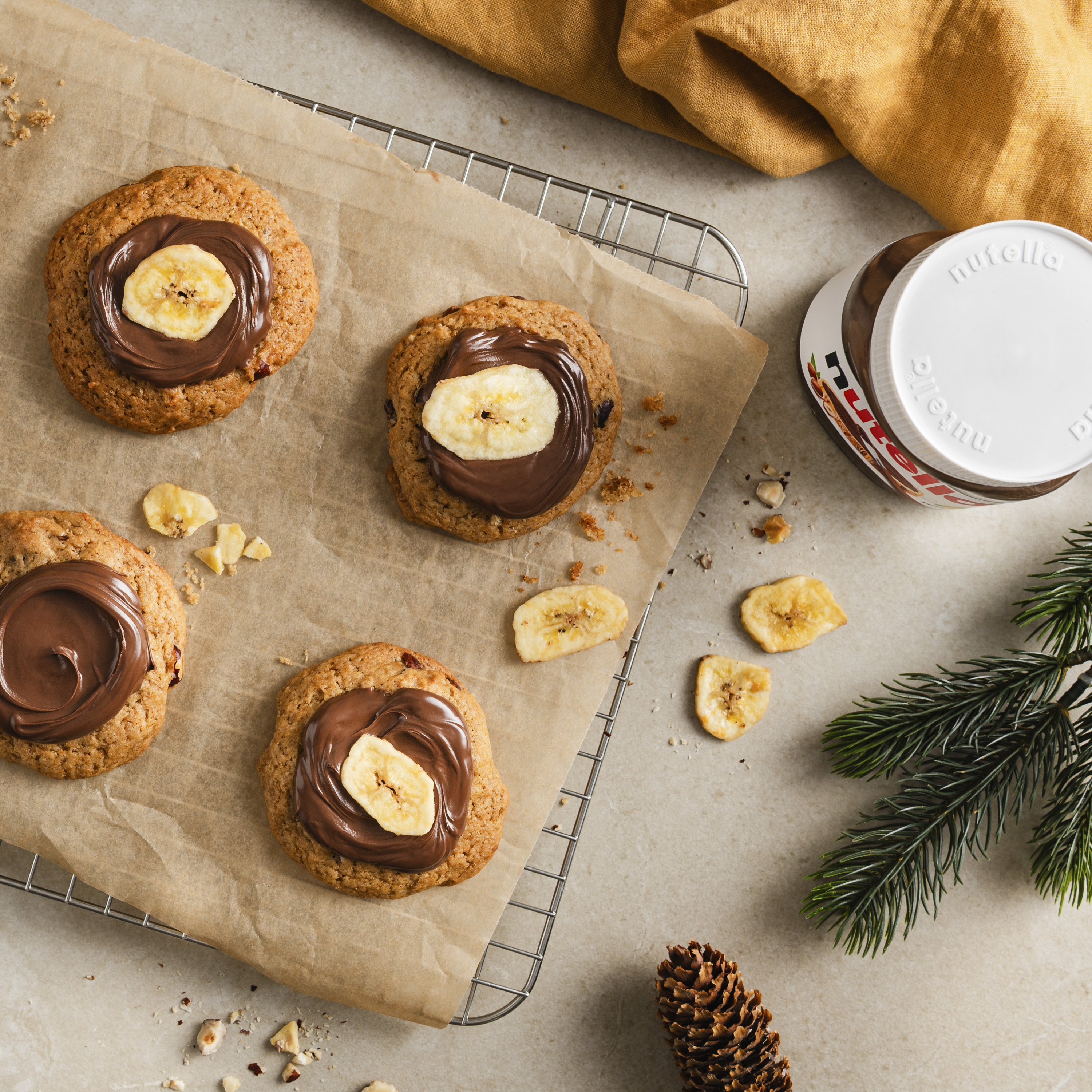Ein Blech mit goldbraunen Cookies, bestrichen mit glänzender Schokocreme, teils garniert mit knusprigen Bananenchips.