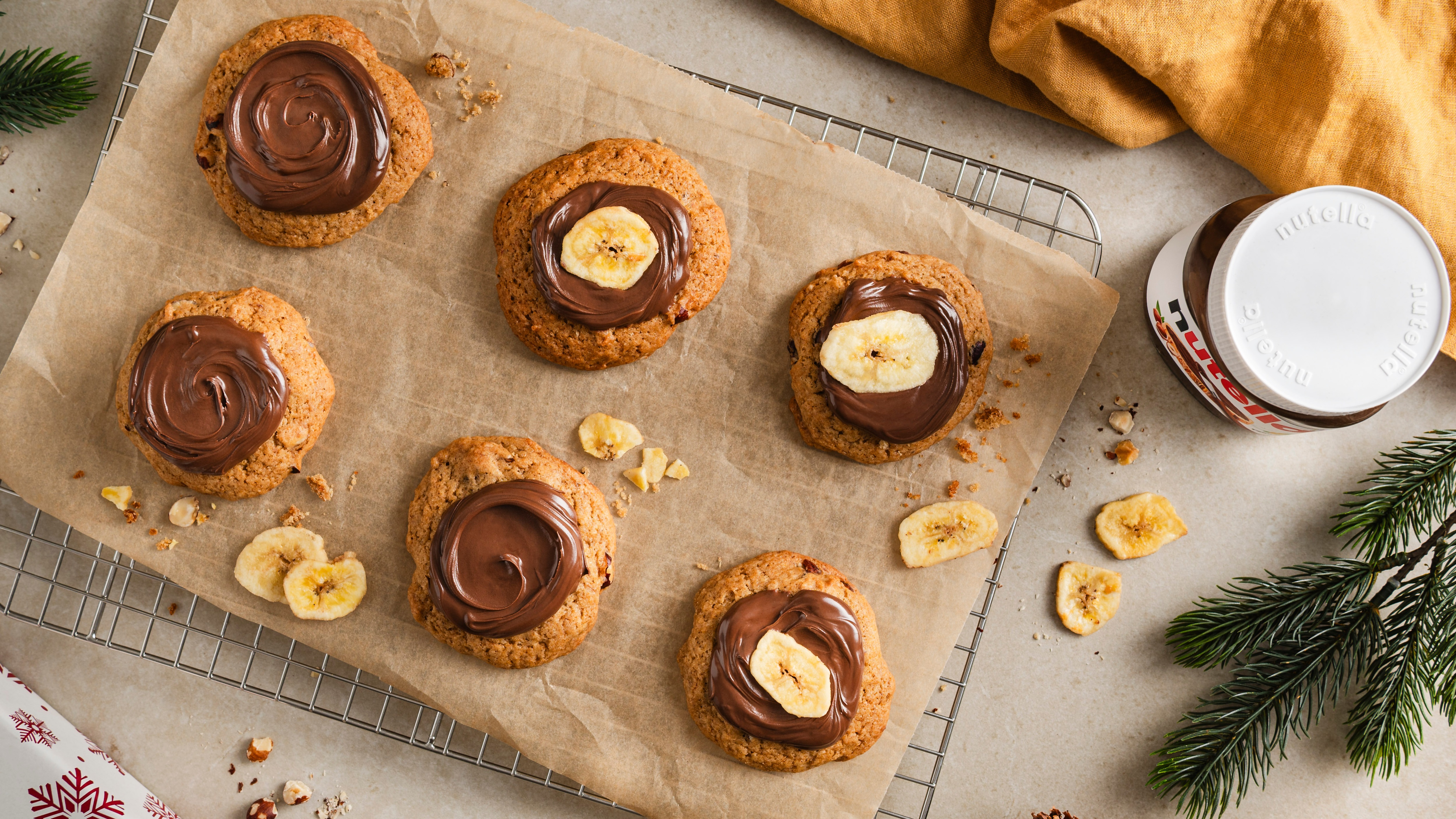 Ein Blech mit goldbraunen Cookies, bestrichen mit glänzender Schokocreme, teils garniert mit knusprigen Bananenchips.