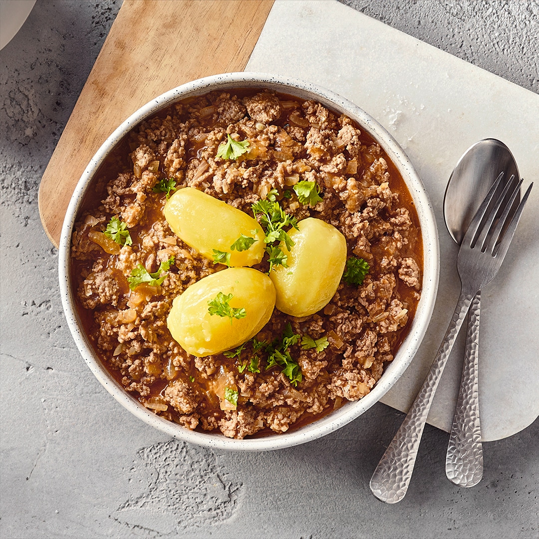Eine Schale mit Hackfleisch in brauner Soße, darauf drei ganze Salzkartoffeln und etwas frische grüne Petersilie als Garnitur