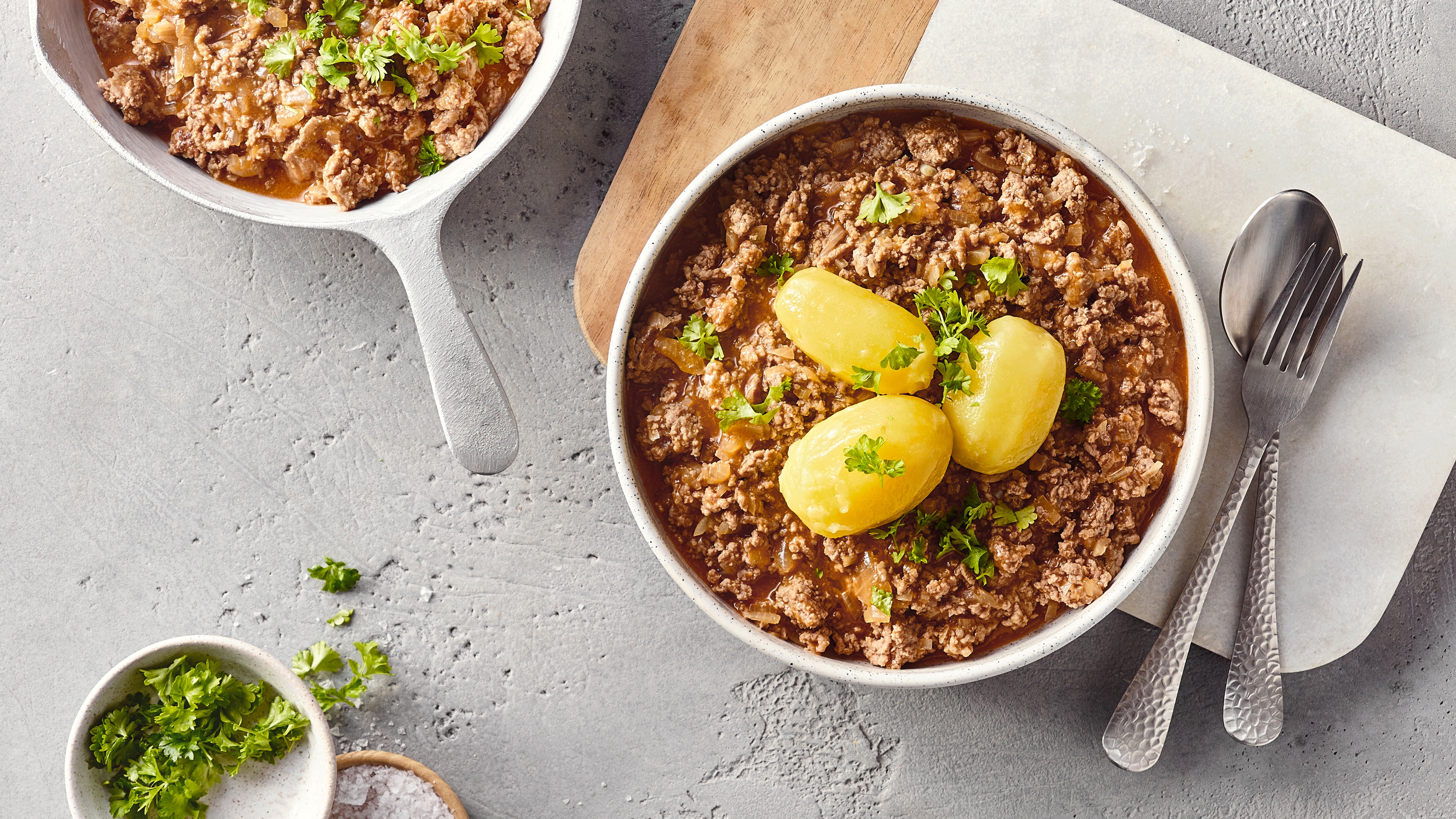Eine Schale mit Hackfleisch in brauner Soße, darauf drei ganze Salzkartoffeln und etwas frische grüne Petersilie als Garnitur