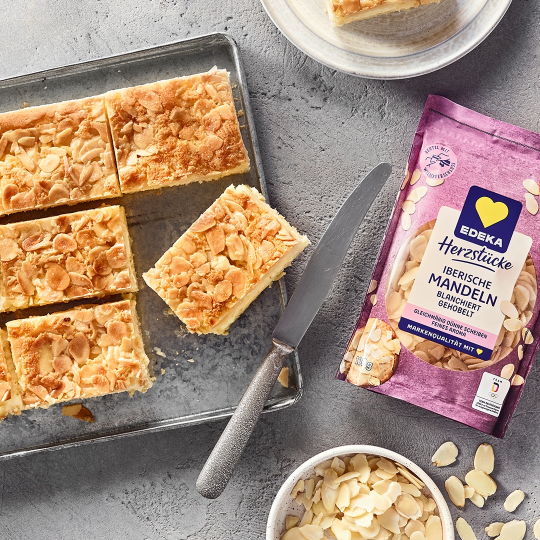 Ein Blech mit rechteckigen Stücken, hellen Schichten und einer Oberfläche aus dünnen, hellbraunen Scheiben und Krümeln.