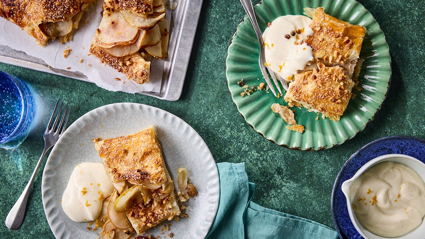 Stücke eines Birnenstrudels mit heller Quarkcreme auf Tellern und Servierplatte.