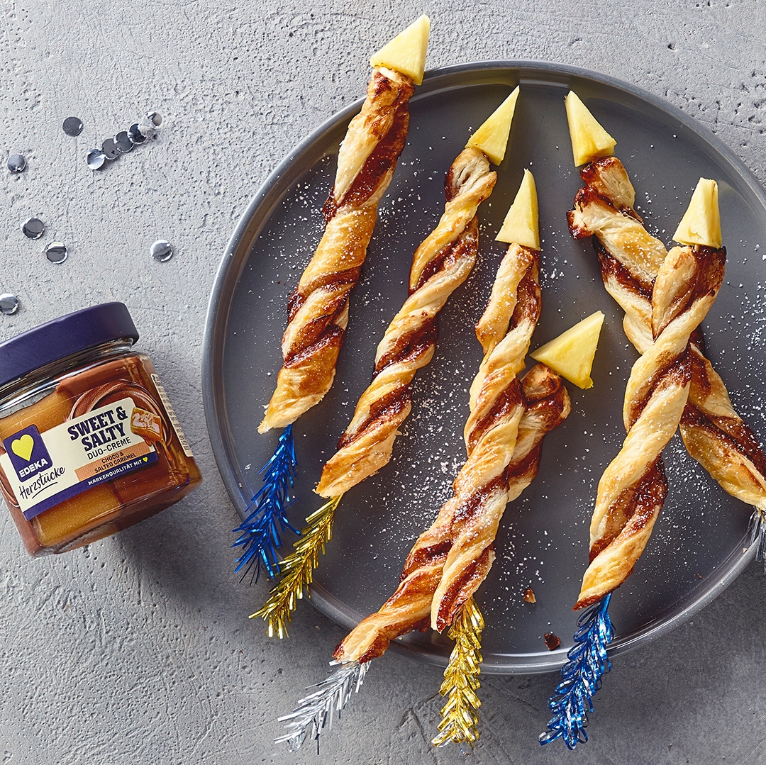 Ein Teller mit sechs gedrehten Blätterteigstangen, gefüllt mit dunkler Creme, bestreut mit Zucker und gelben Spitzen