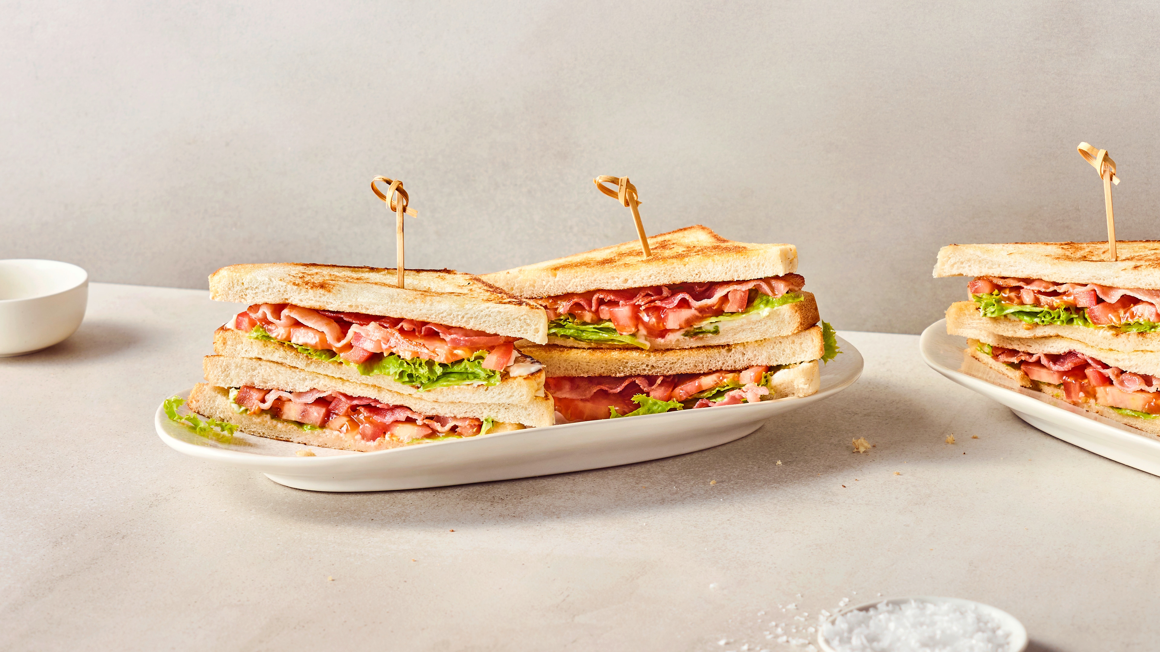Ein ovaler Teller mit getoasteten Doppeldecker-Sandwiches, belegt mit Schinken, Tomatenscheiben und frischem Salat