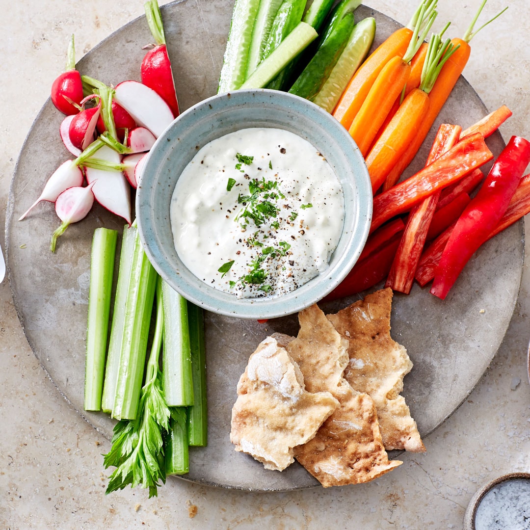 Cremiger heller Dip in kleinem Schälchen, umrundet von Rohkost und Crackern