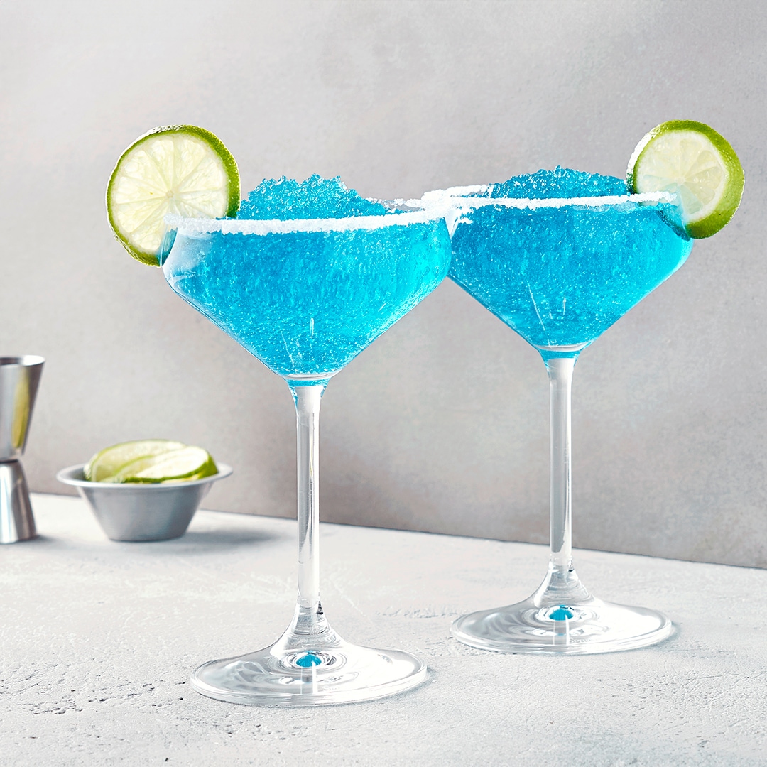 Zwei Martinigläser mit hellblauer Flüssigkeit aus Eis, garniert mit Limettenscheiben