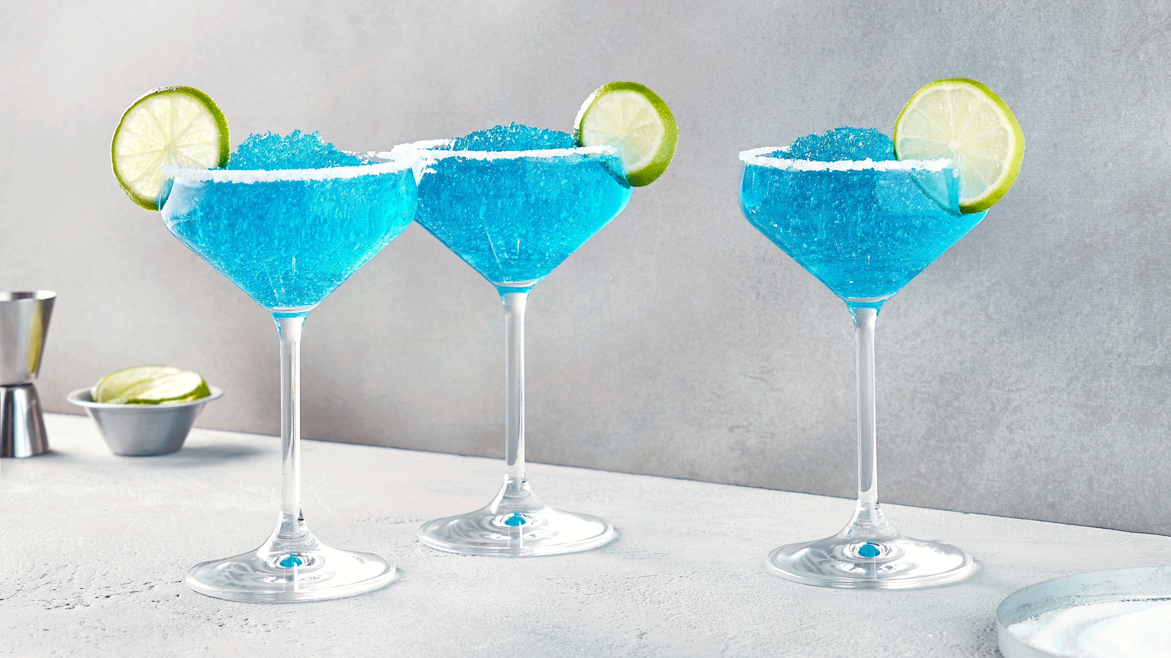 Drei Martinigläser mit hellblauer Flüssigkeit aus Eis, garniert mit Limettenscheiben