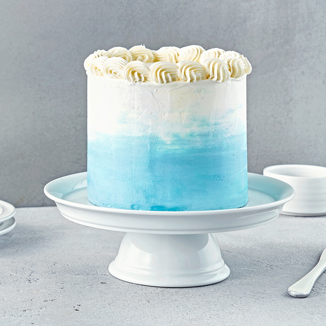 Eine hohe weiß-hellblaue Torte mit Sahnetupfern auf einer Etagere