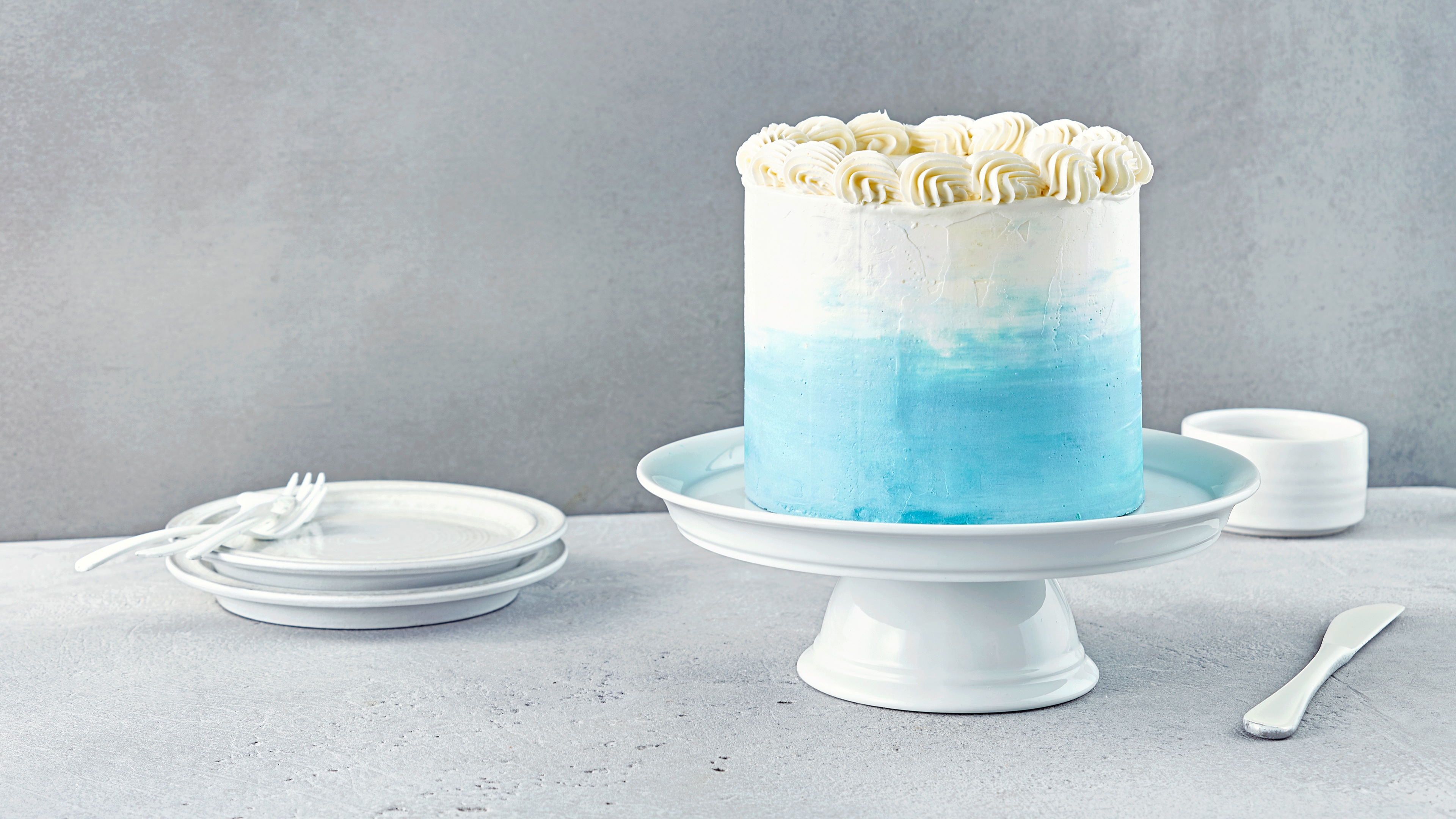 Eine hohe weiß-hellblaue Torte mit Sahnetupfern auf einer Etagere