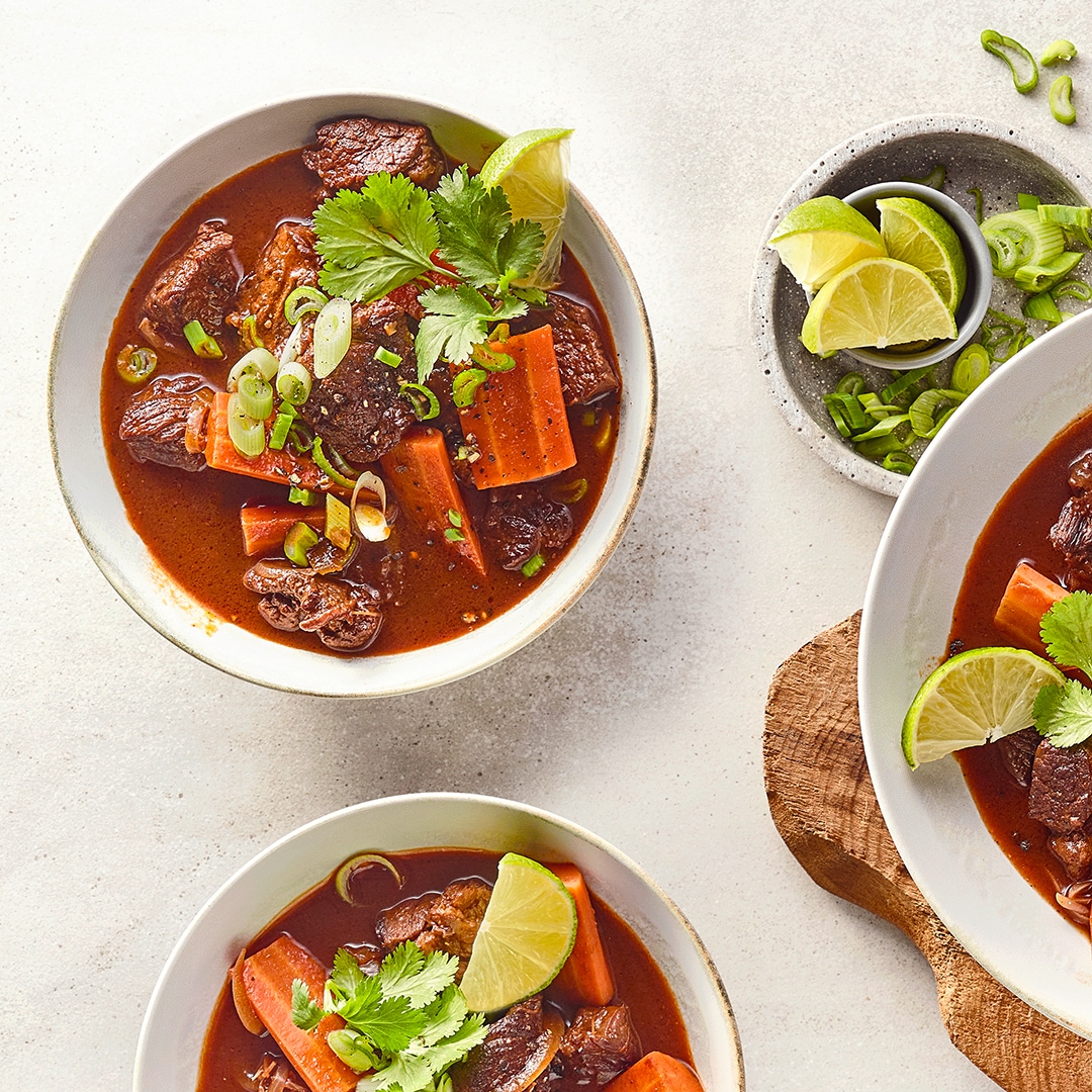 Schalen mit dunkler Brühe, Fleischstücken, Möhrenstücken und Kräutern