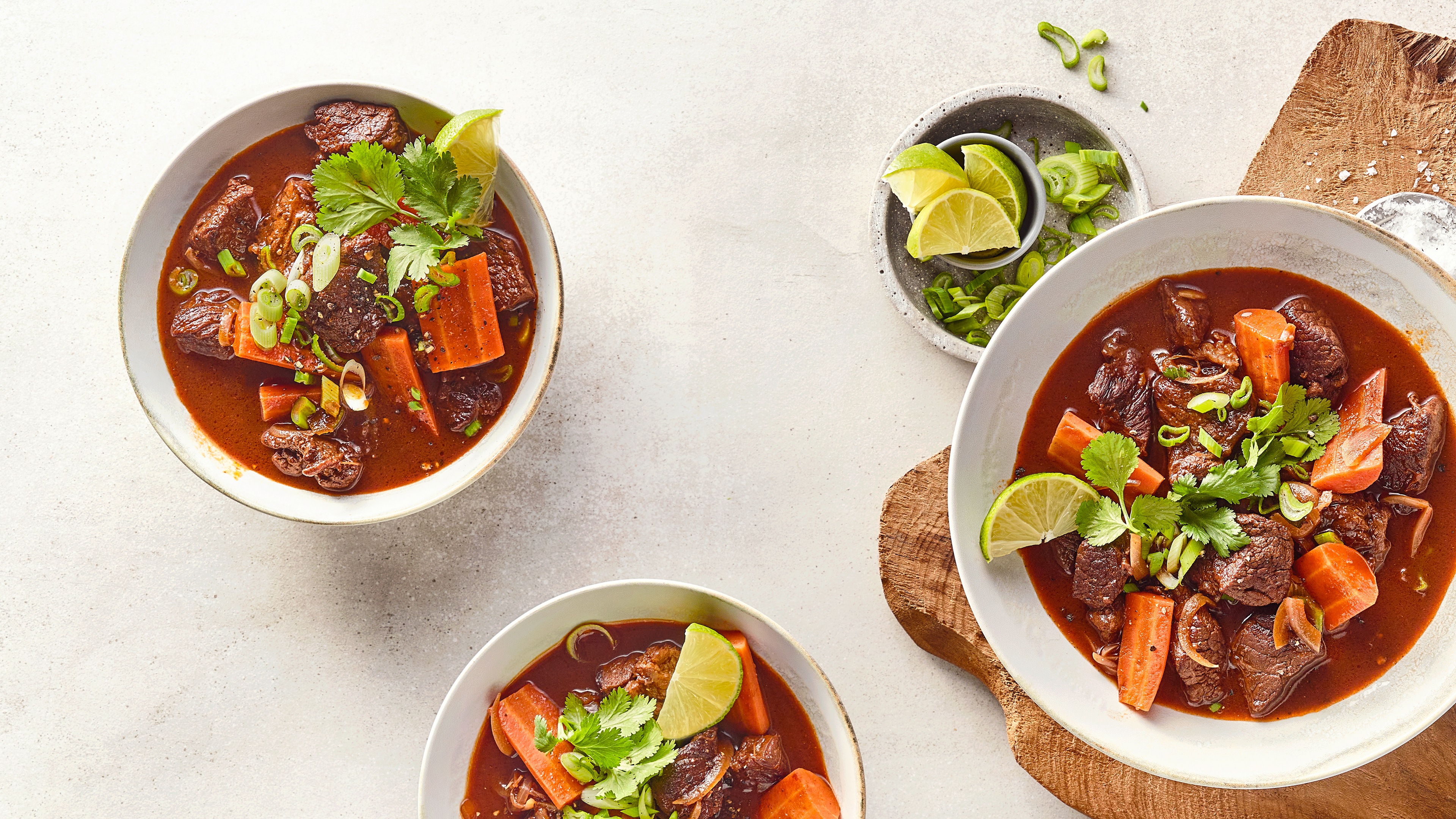 Schalen mit dunkler Brühe, Fleischstücken, Möhrenstücken und Kräutern