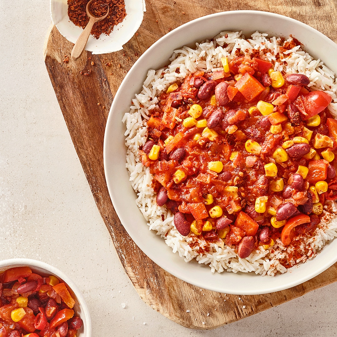 Eine Schüssel mit weißem Reis, darauf rote Soße mit Mais, roten Bohnen und Stücken von rotem Gemüse.
