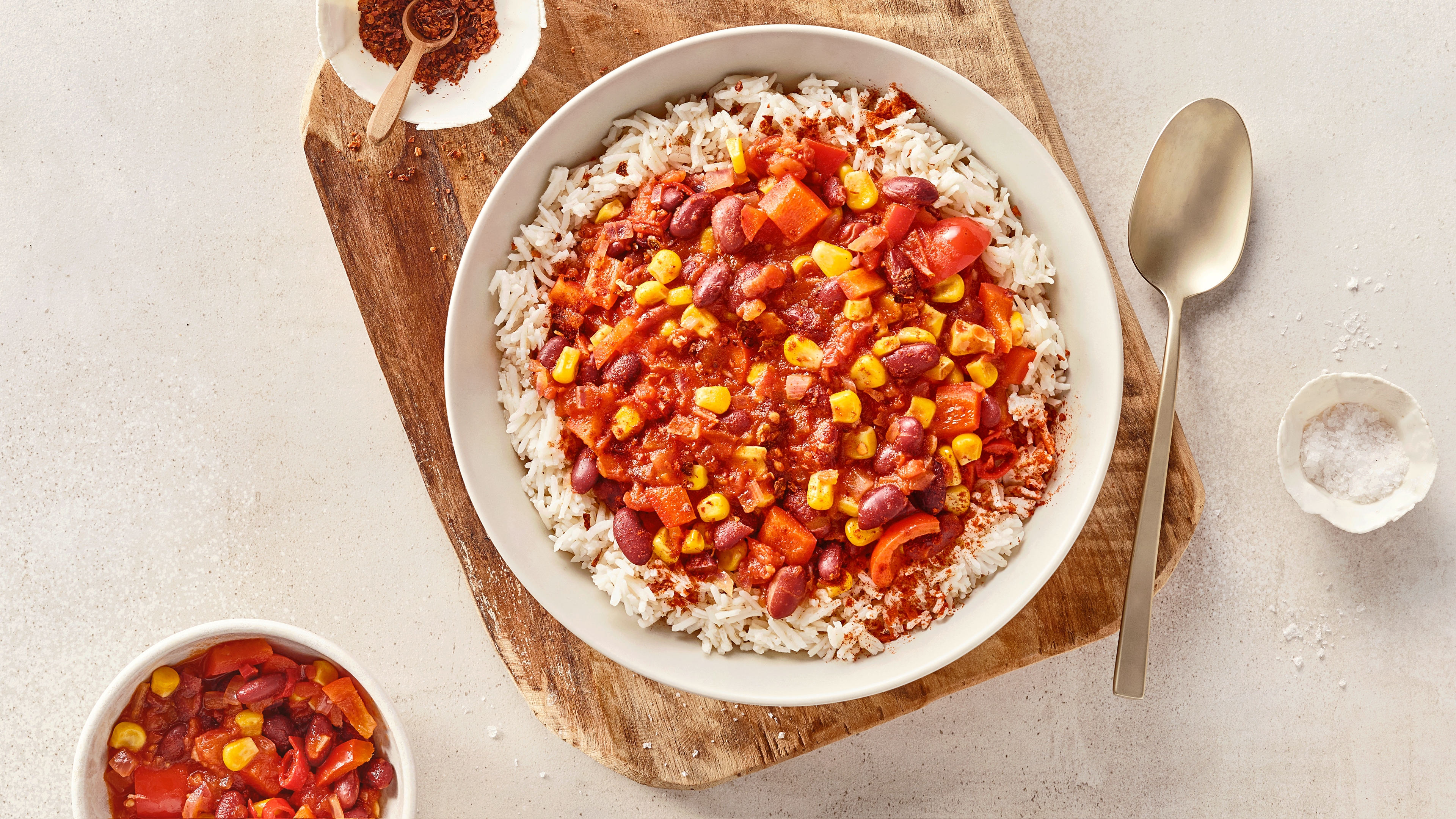 Eine Schüssel mit weißem Reis, darauf rote Soße mit Mais, roten Bohnen und Stücken von rotem Gemüse.