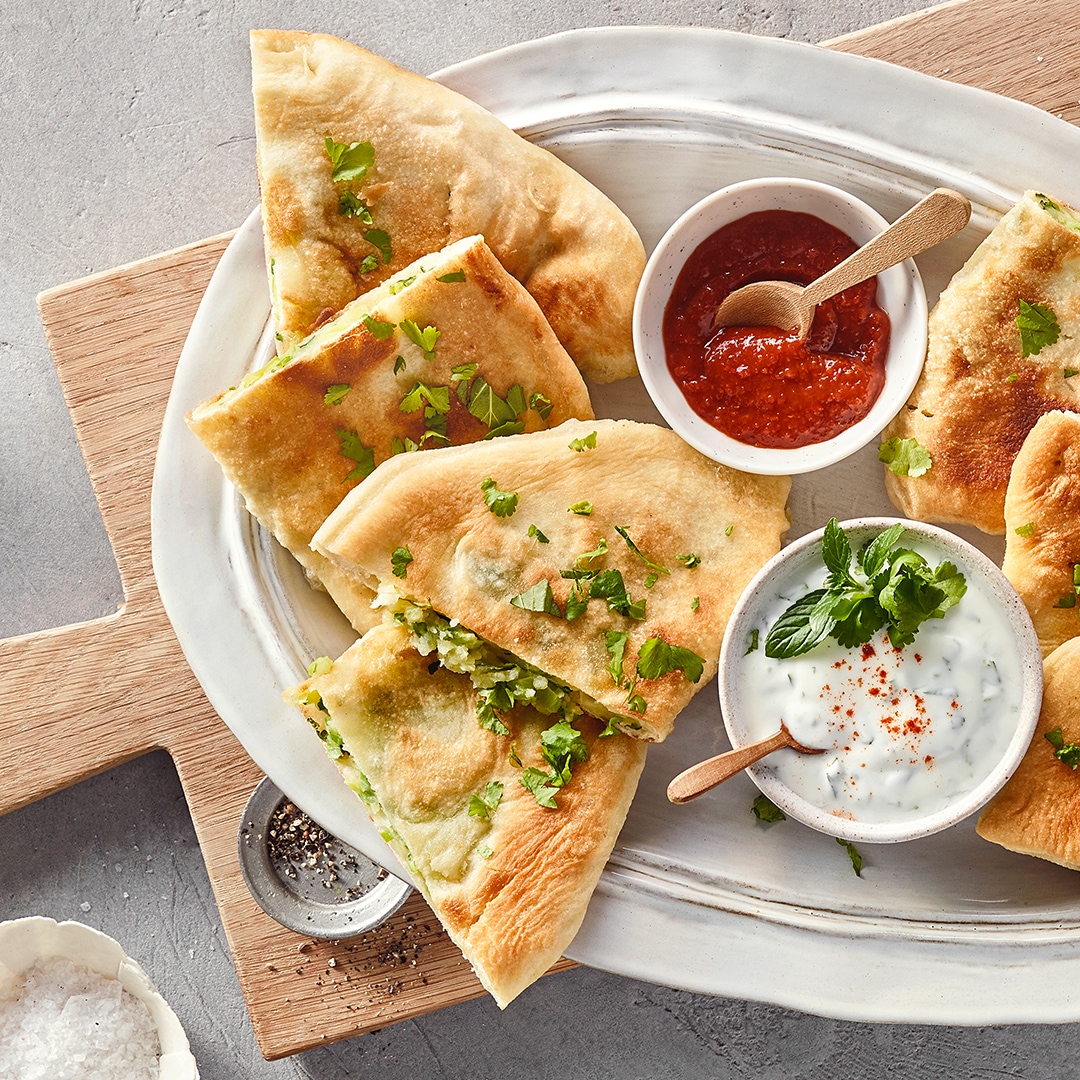 Mit Kräutern garnierte Teigfladen mit hellem und rotem Dip auf großem Teller