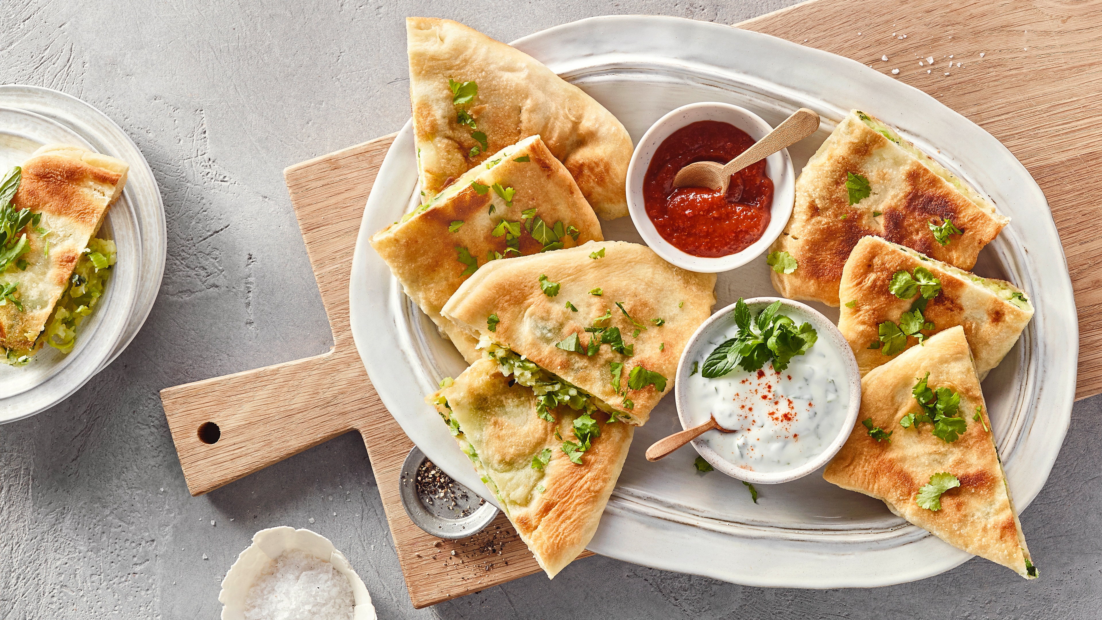 Mit Kräutern garnierte Teigfladen mit hellem und rotem Dip auf großem Teller