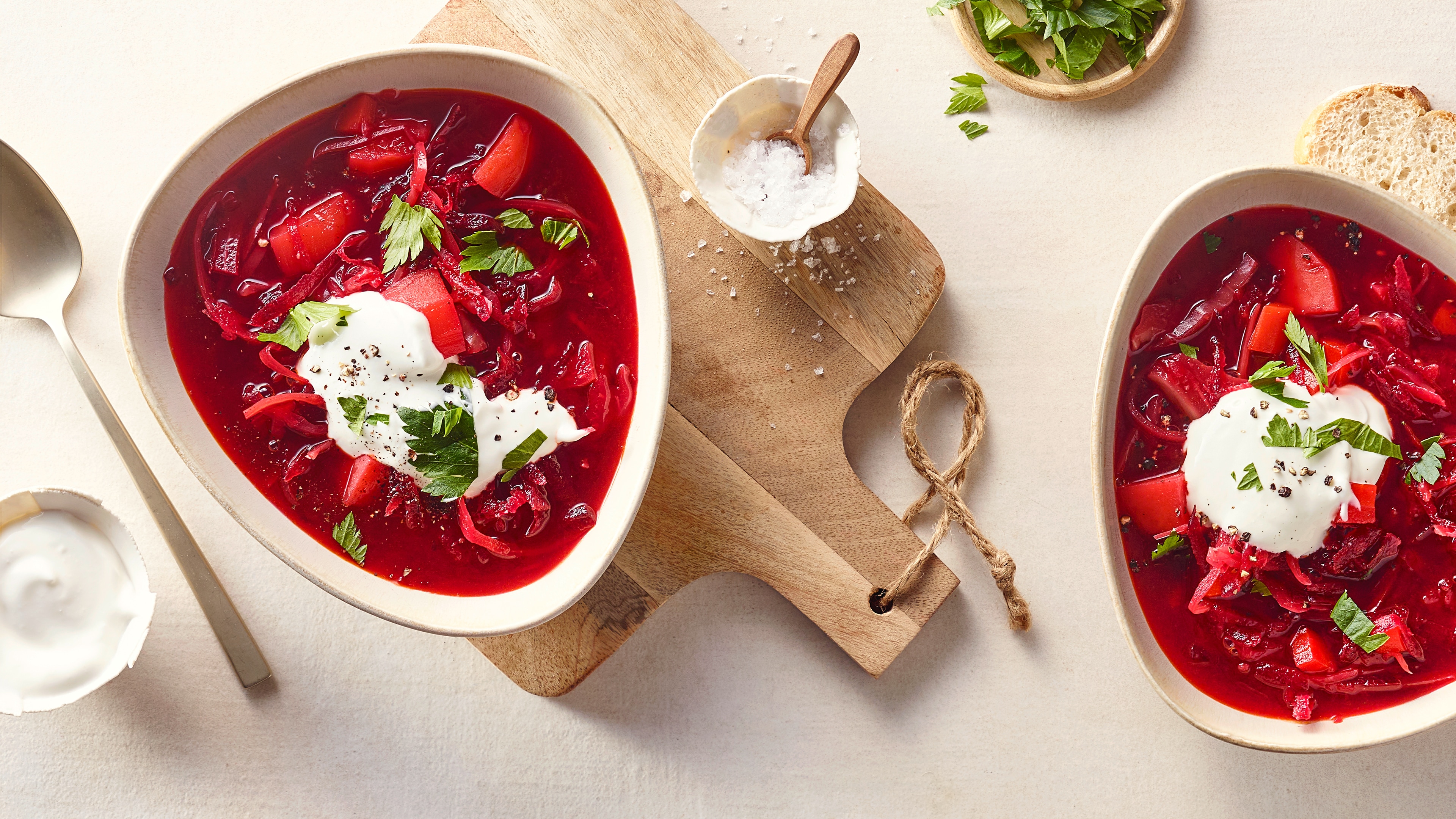 Eine Schale mit roter Suppe aus Rote Bete und Gemüse, garniert mit einem Klecks weißer Creme und frischen grünen Kräutern