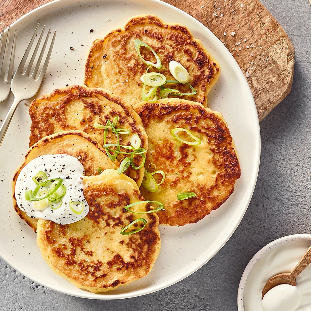 Ein Teller mit vier runden, goldbraunen Stücken, grünen Ringen und einem weißen Klecks mit schwarzen Punkten auf einem Stück.