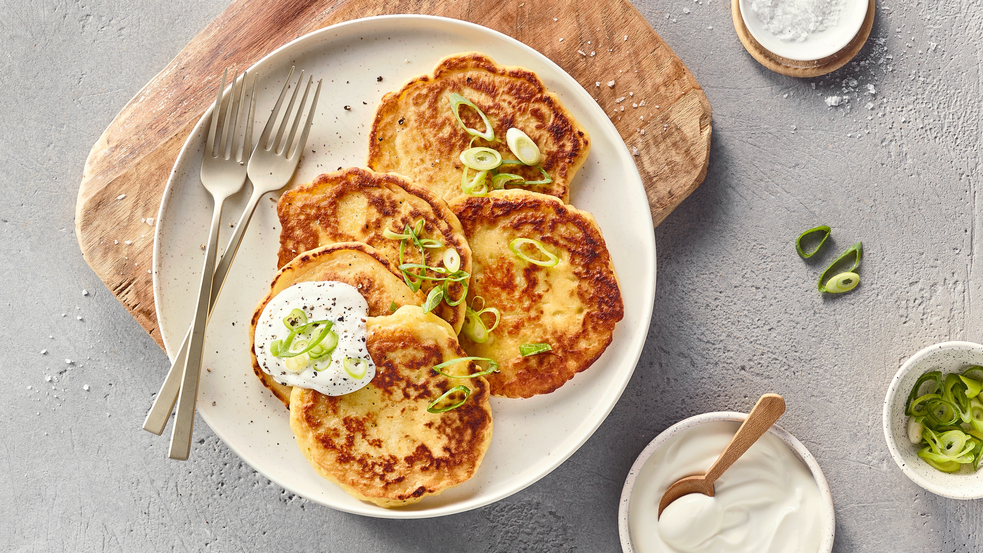 Ein Teller mit vier runden, goldbraunen Stücken, grünen Ringen und einem weißen Klecks mit schwarzen Punkten auf einem Stück.