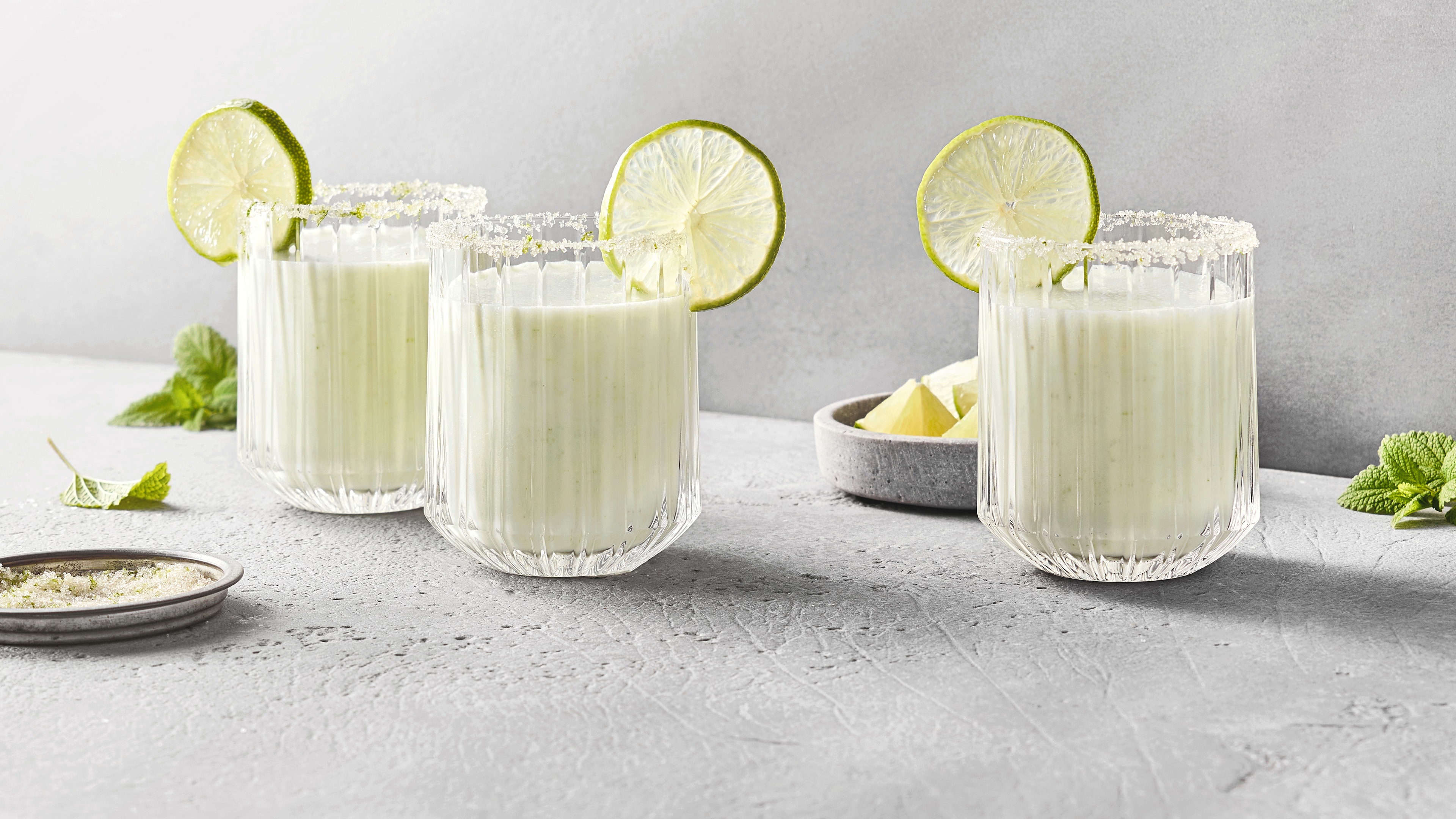 Drei Gläser mit cremiger Limonade, mit Limettenscheiben serviert.