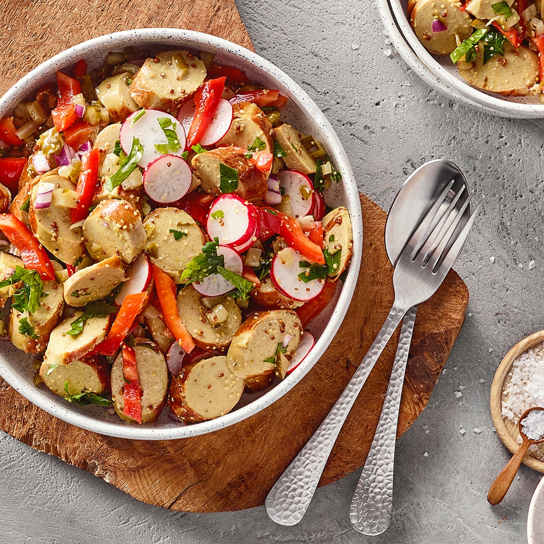 Schale auf Holzbrett mit Bratwurststücken, Radieschenscheiben, Paprikastücken und Kräutern