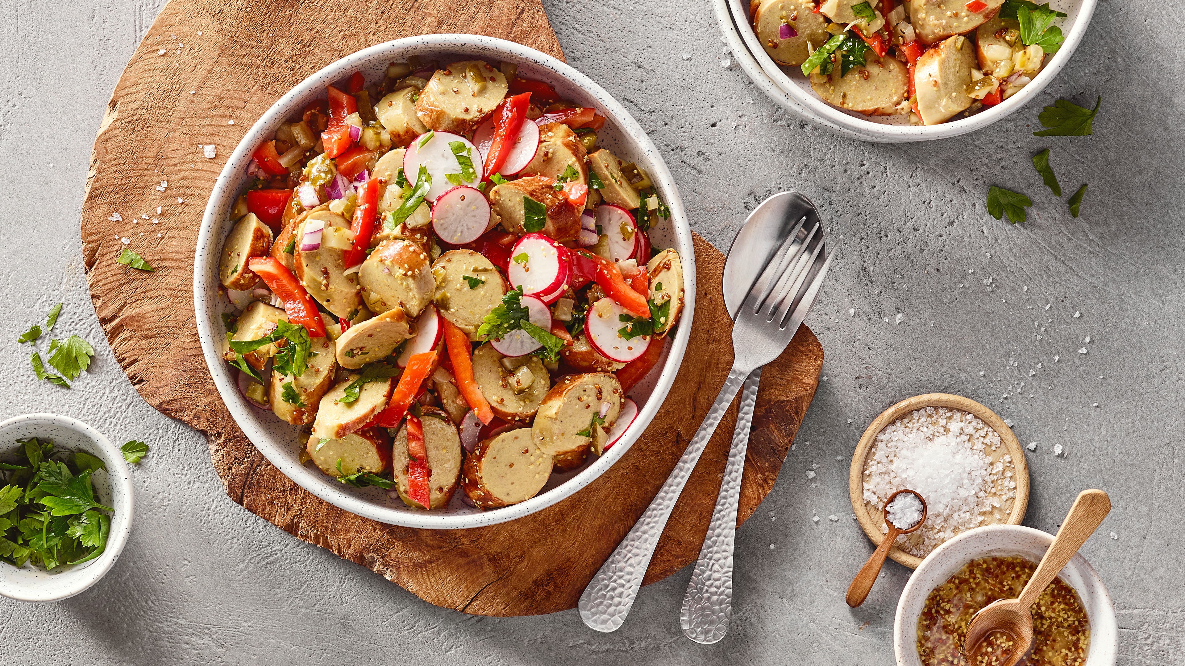 Schale auf Holzbrett mit Bratwurststücken, Radieschenscheiben, Paprikastücken und Kräutern