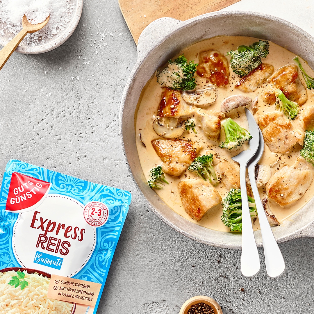 Pfanne mit cremigem Gericht aus gebratenen Hähnchenstücken und Brokkoli, serviert mit einer Schüssel Reis. Daneben GUT&GÜNSTIG Express Reis Basmati.