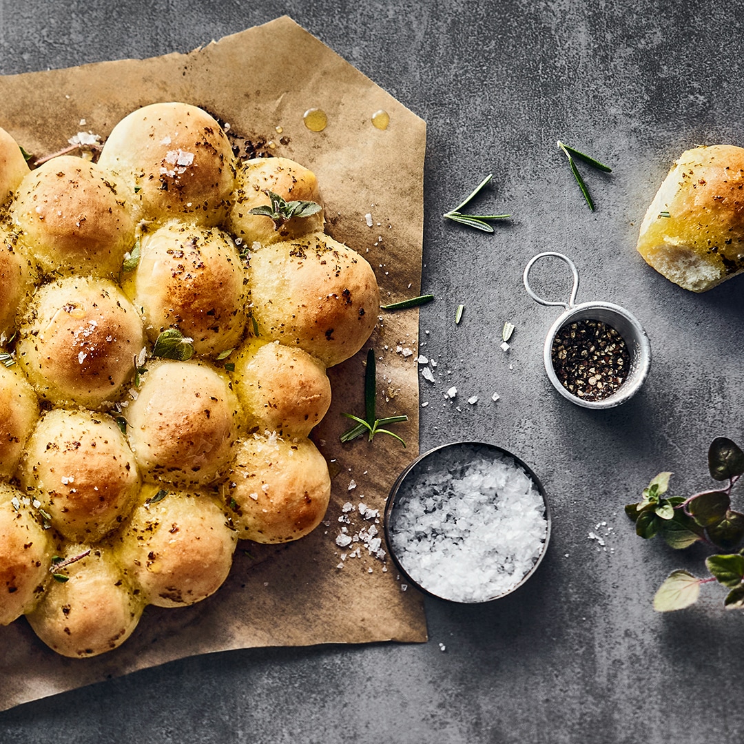 Ein fluffiges, gelbgoldenes, hügeliges Brot mit Kräuterbutter, getoppt mit frischem Oregano auf Backpapier