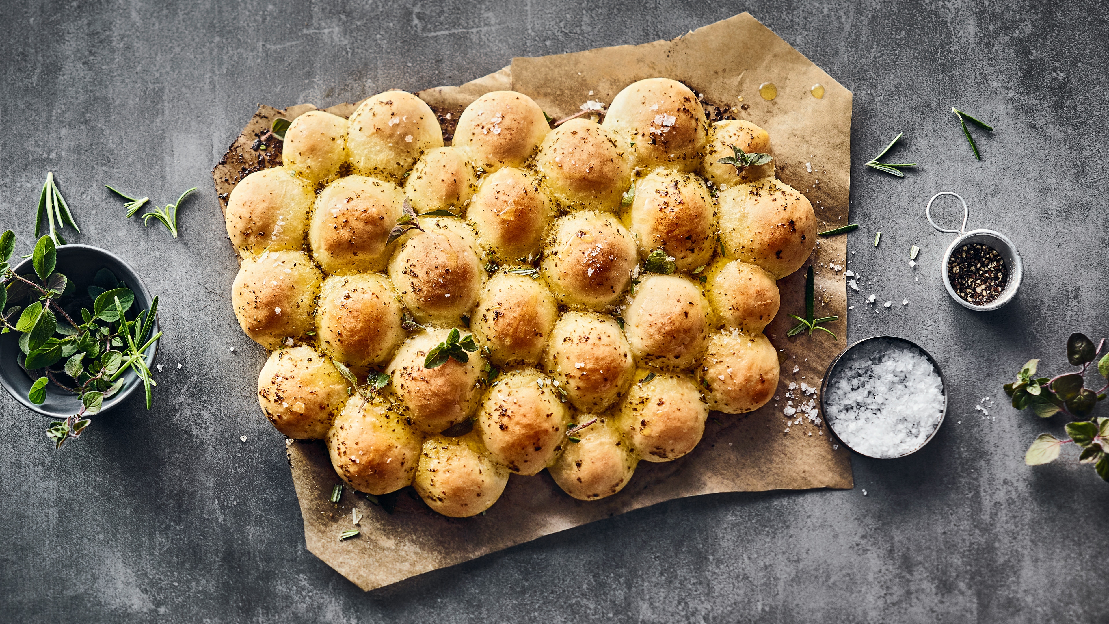 Ein fluffiges, gelbgoldenes, hügeliges Brot mit Kräuterbutter, getoppt mit frischem Oregano auf Backpapier