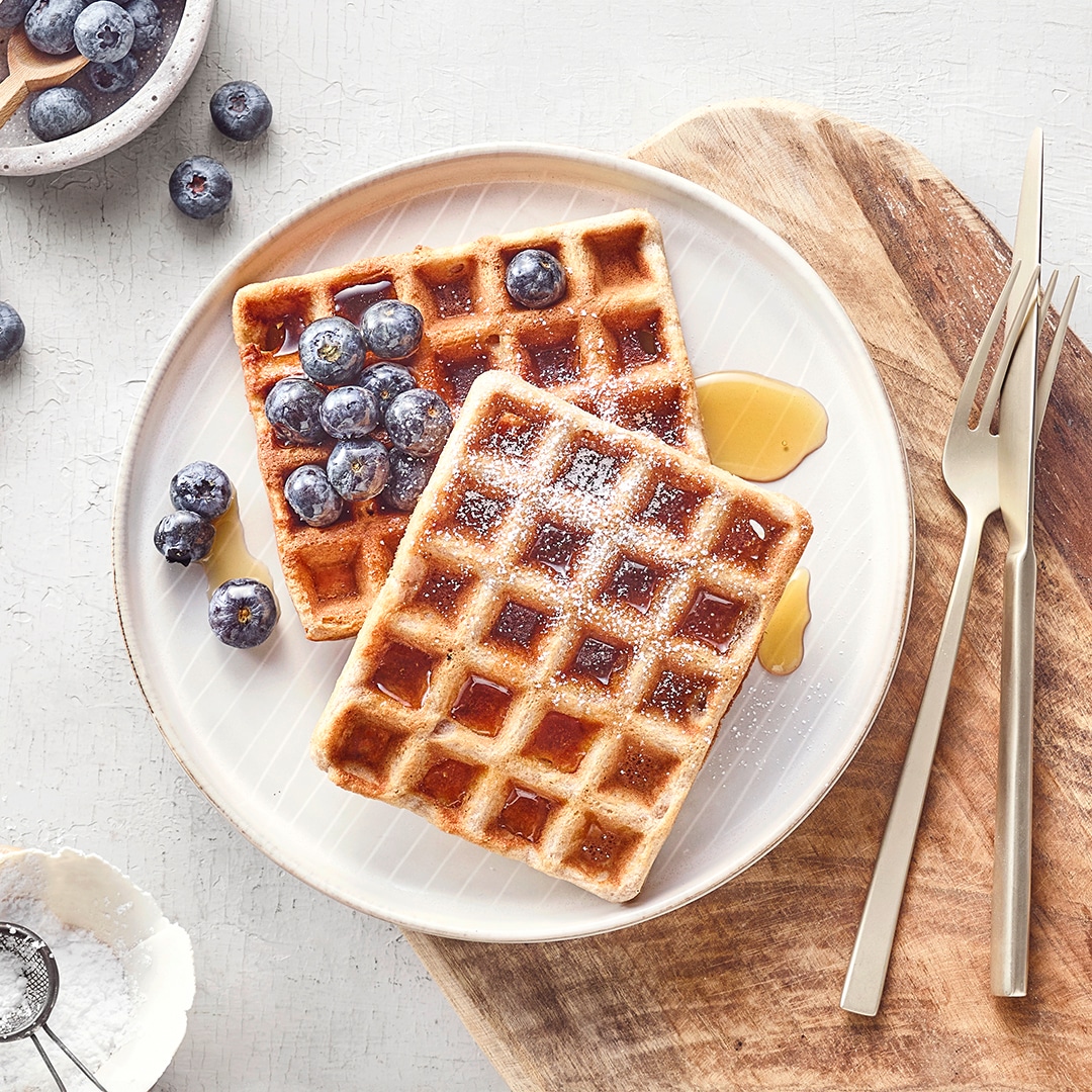 Zwei dunkle Waffeln, verziert mit Blaubeeren, Ahornsirup und Puderzucker.