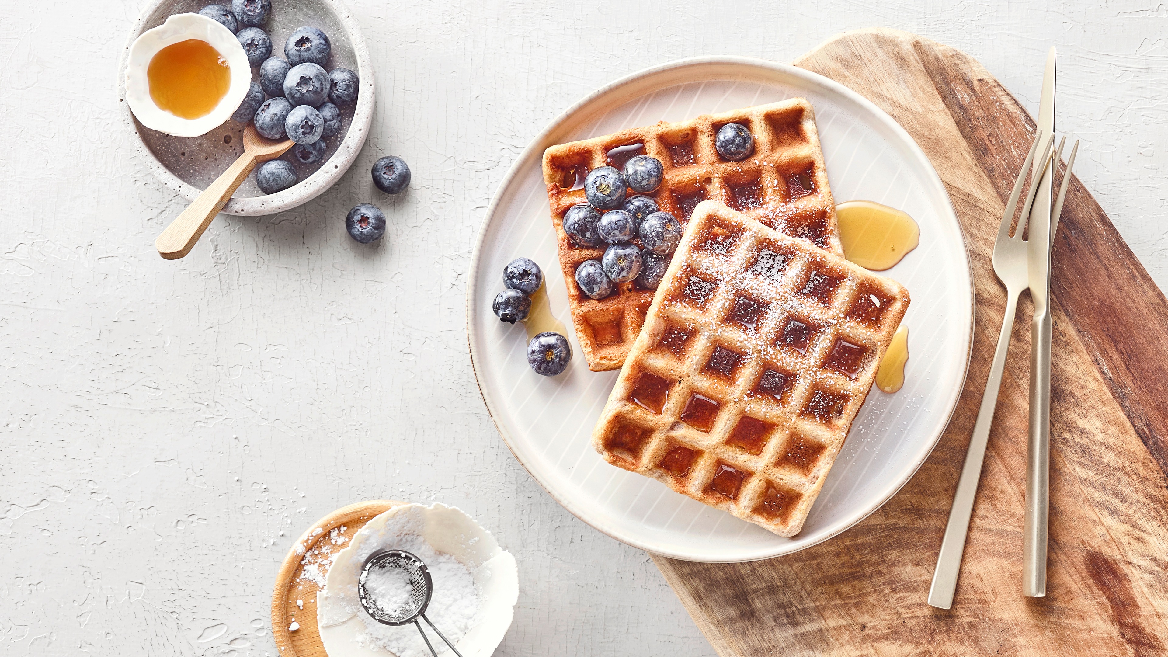 Zwei dunkle Waffeln, verziert mit Blaubeeren, Sirup und Puderzucker.