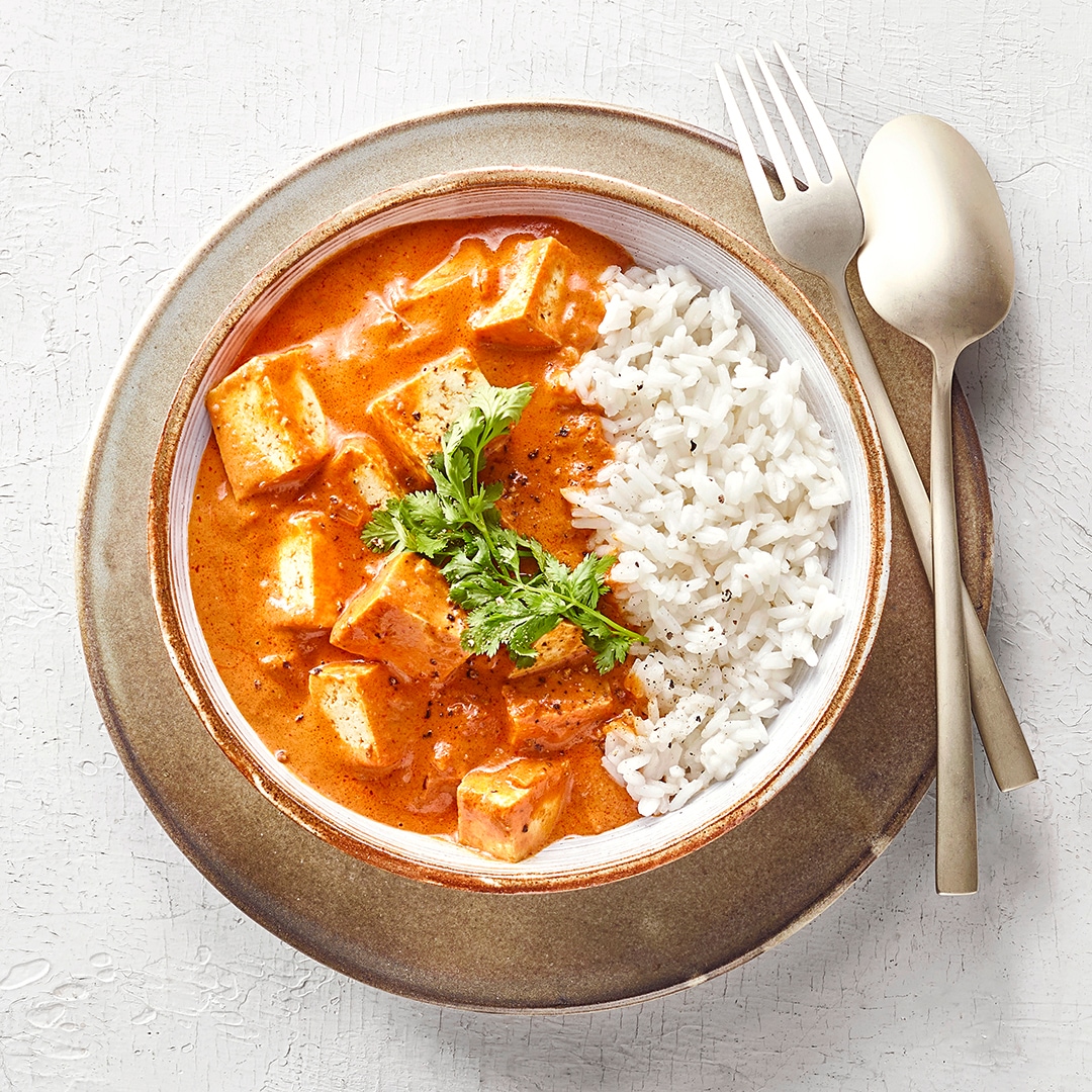 Schüssel mit Reis sowie Hähnchen mit einer cremigen Tomatensauce.
