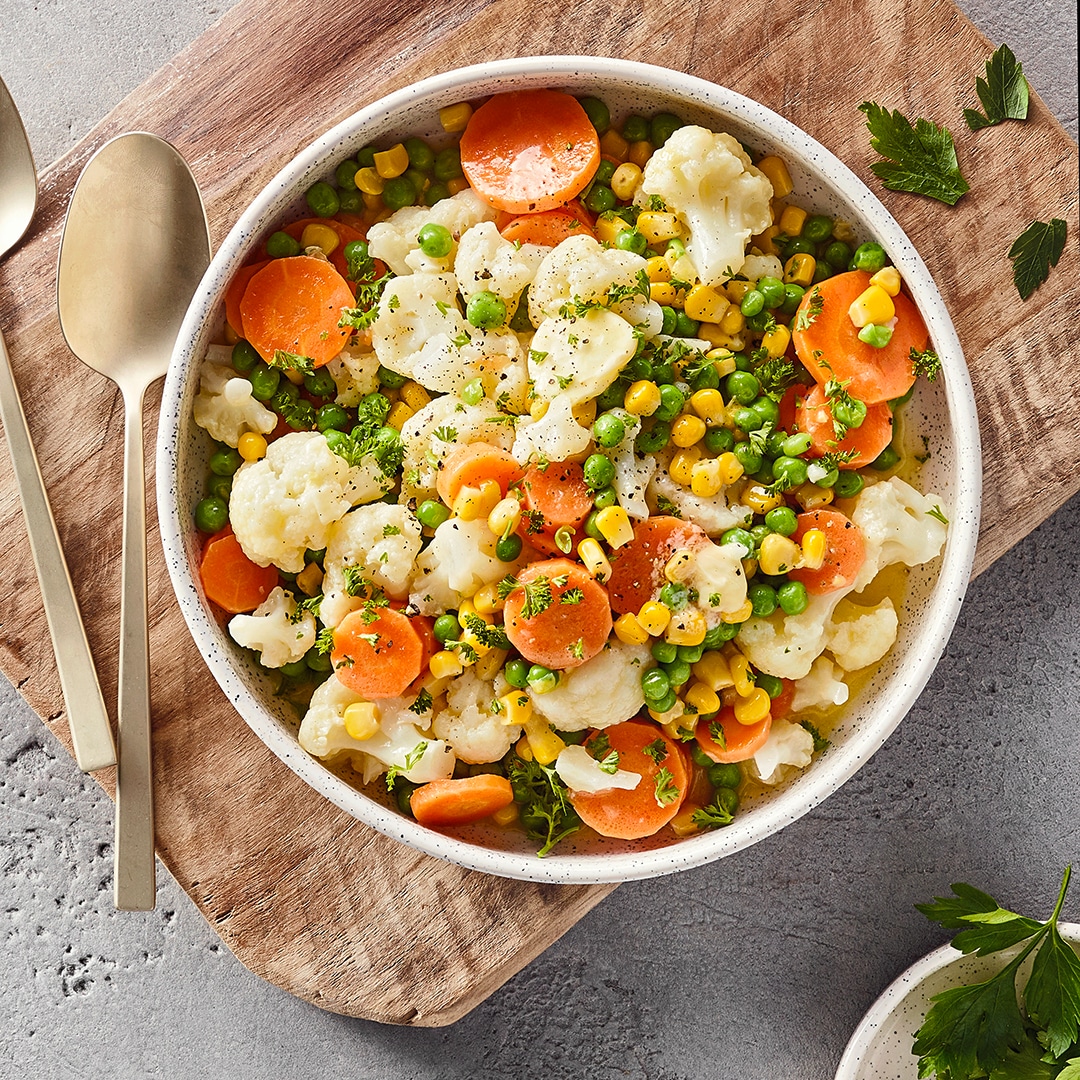 Schale mit Blumenkohlröschen, Möhrenscheiben, Erbsen und Mais. Mit Kräutern garniert.