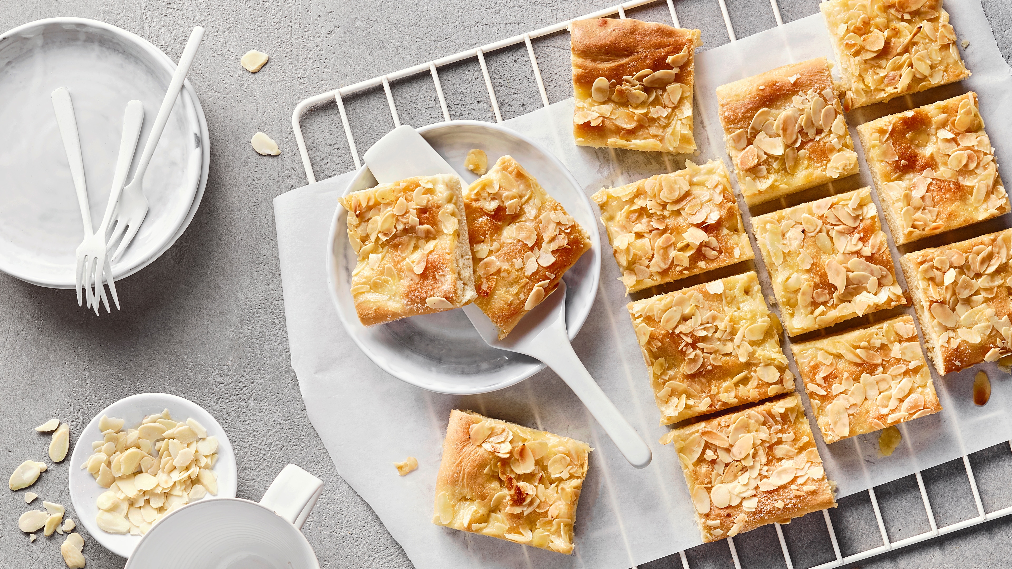 Ein Teller mit mehreren rechteckigen Kuchenstücken, belegt mit hellen Mandelblättchen auf einem goldenen Teig.