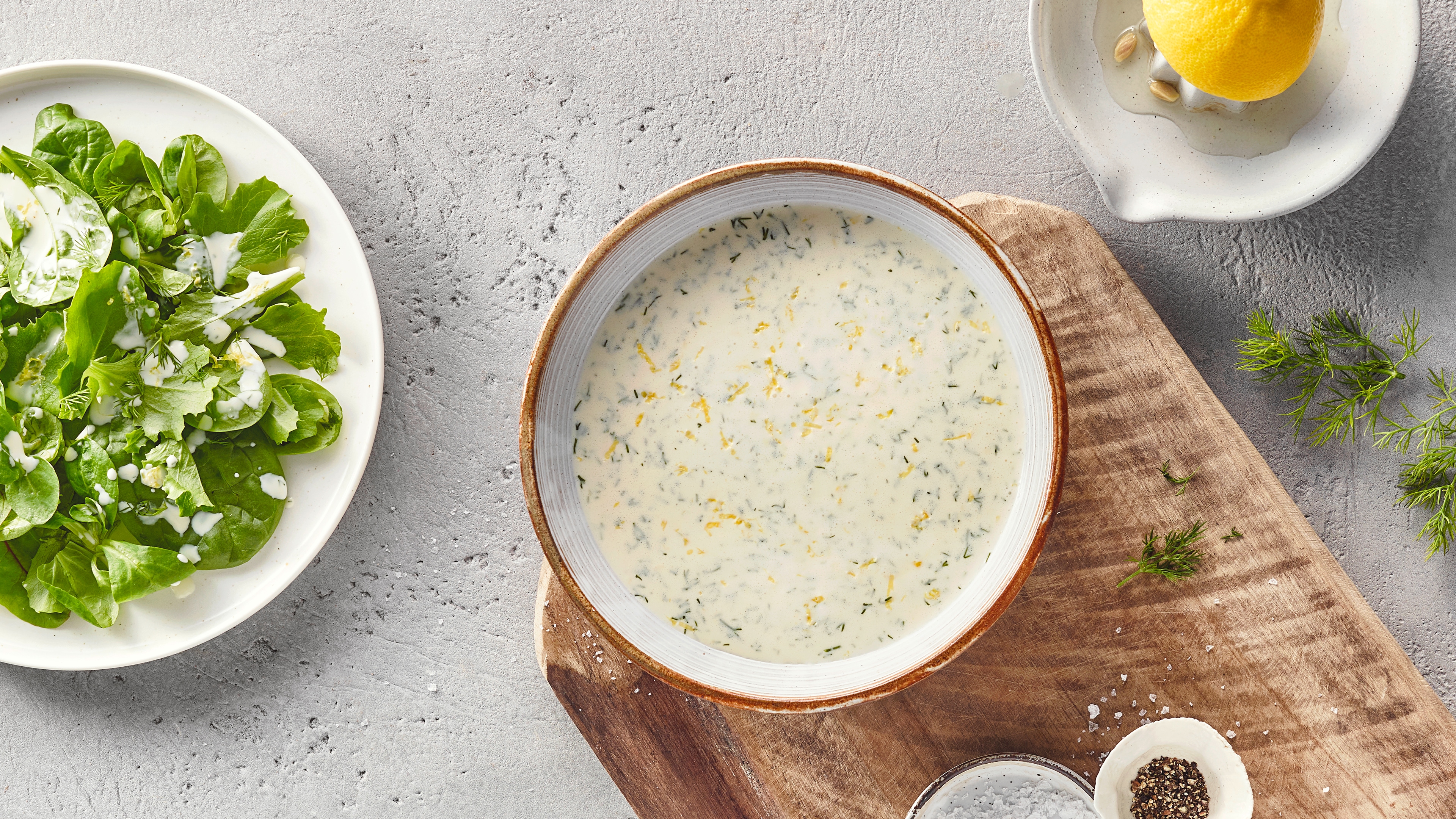 Eine Schale mit heller, cremiger Flüssigkeit, durchzogen von feinen grünen Kräuterstücken und kleinen gelben Streifen.