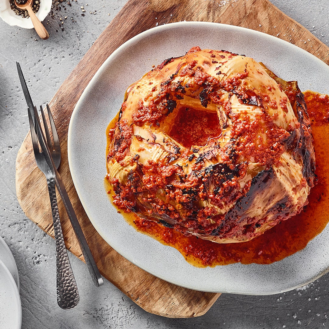 Ein Teller mit einem gebackenen Kohlkopf, bedeckt mit roter Soße und kleinen Körnern.