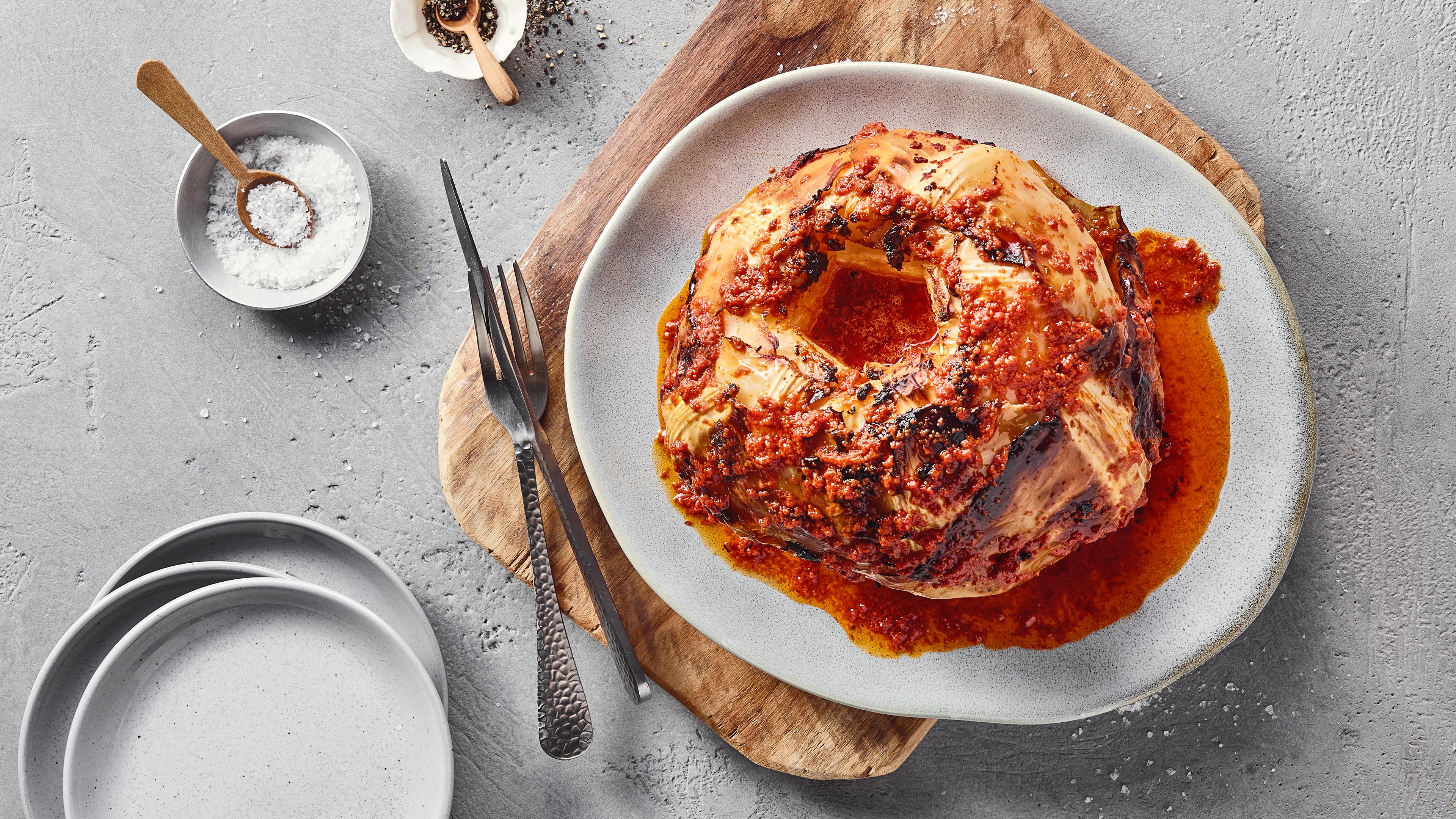 Ein Teller mit einem gebackenen Kohlkopf, bedeckt mit roter Soße und kleinen Körnern.