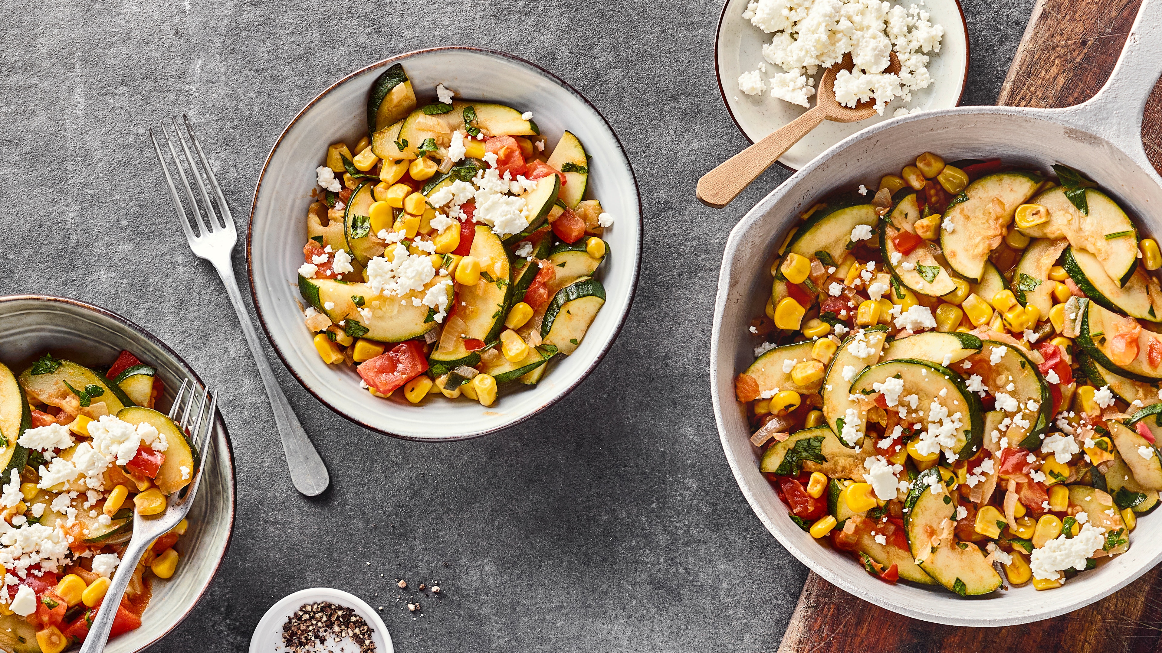 Rezept für spanische Calabacitas Runde Schälchen mit Mais, Zucchini- und Paprikastückchen, getoppt mit Schafskäsebröseln und gehacktem Koriander