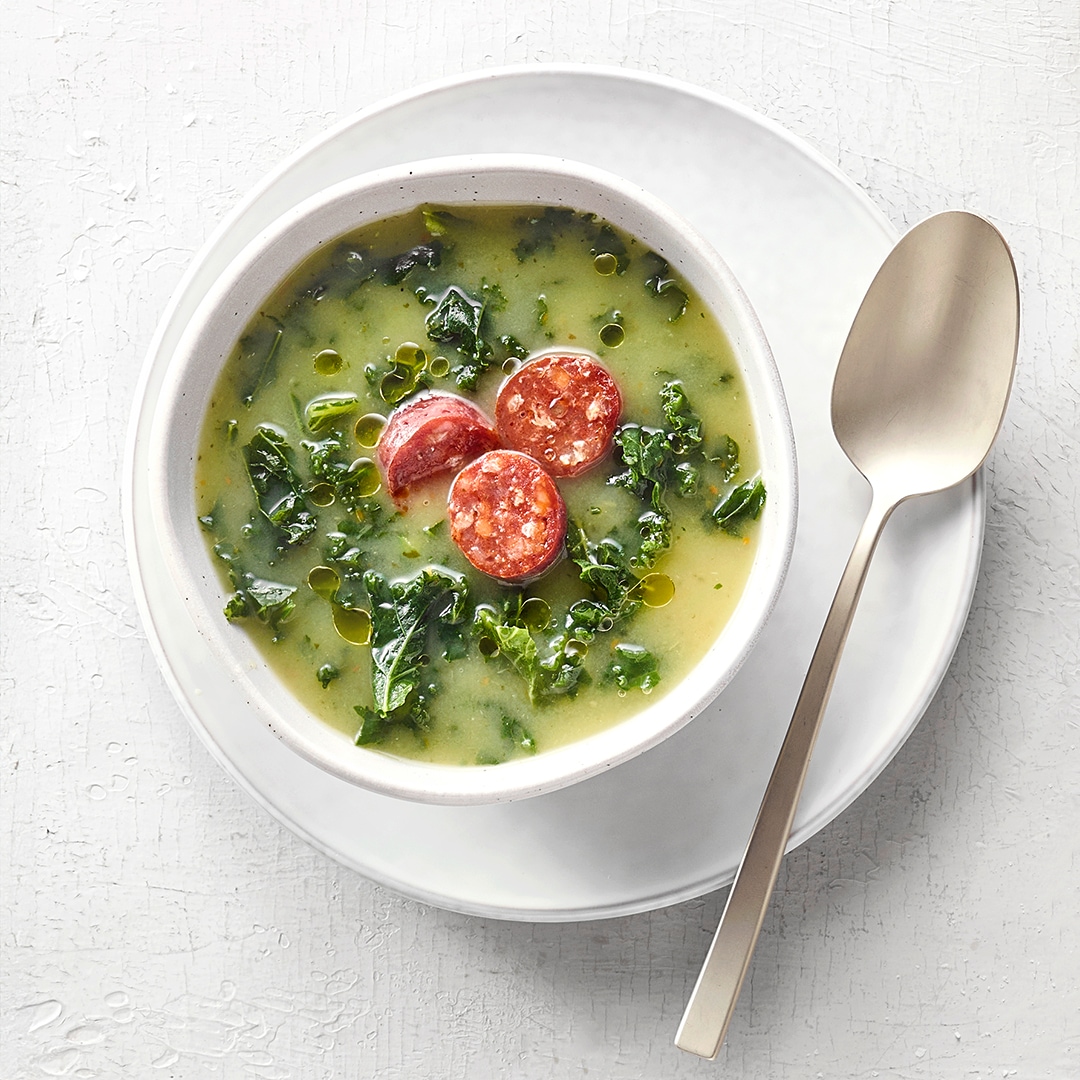 Schüssel mit grüner, kohliger Suppe und kleinen, runden Fleischscheiben.