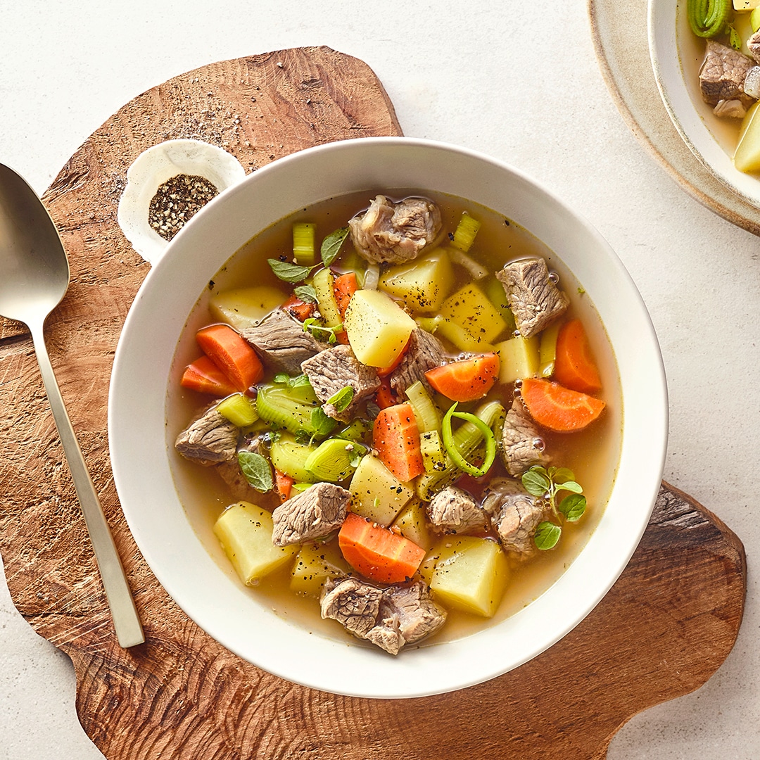 Tiefer Teller mit Kartoffel-, Möhren und Fleischstücken in Brühe