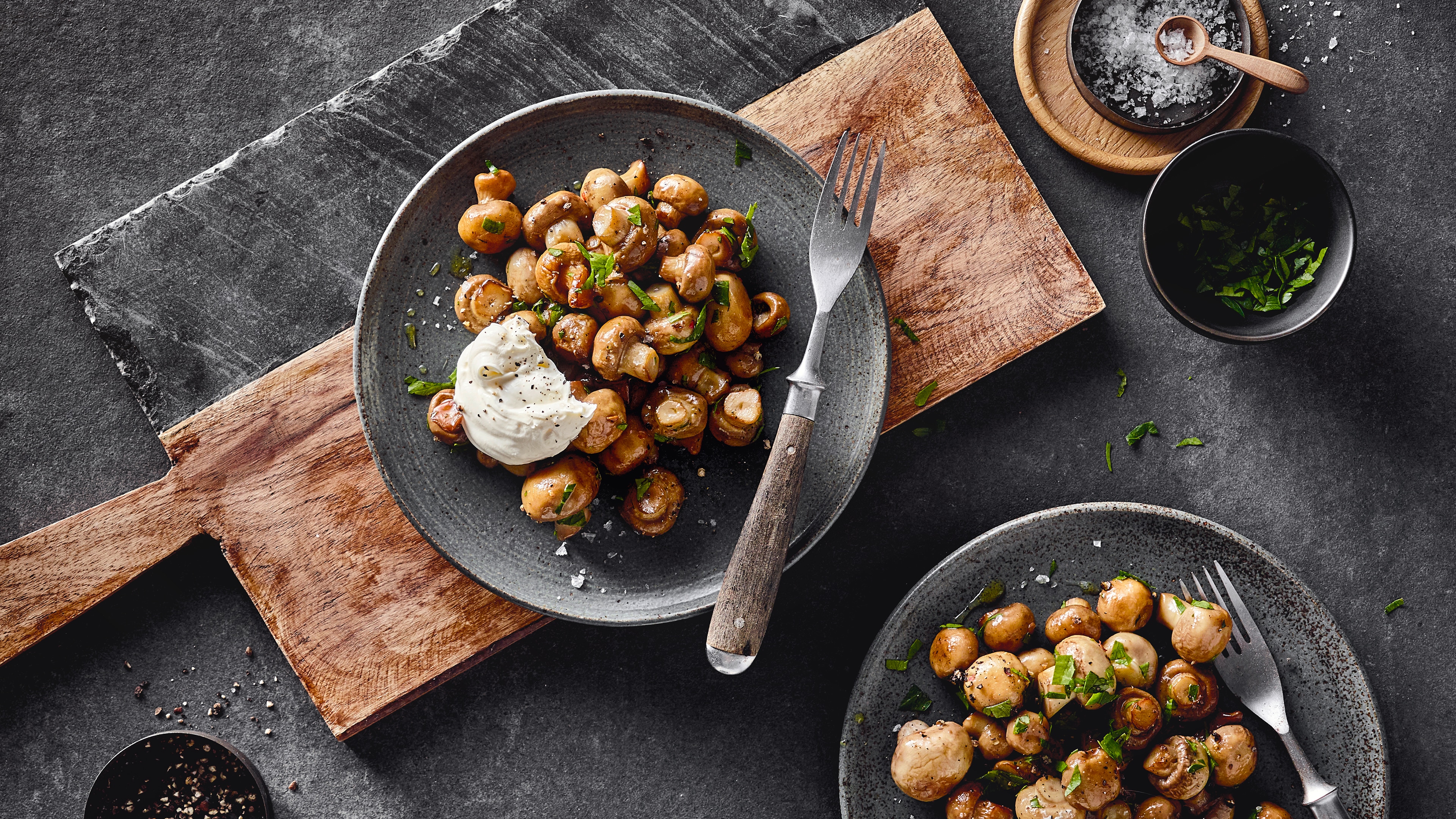 Ein rustikaler Teller mit kleinen Champignons, getoppt mit einem Klecks weißer creme und frischen gehackten Kräutern